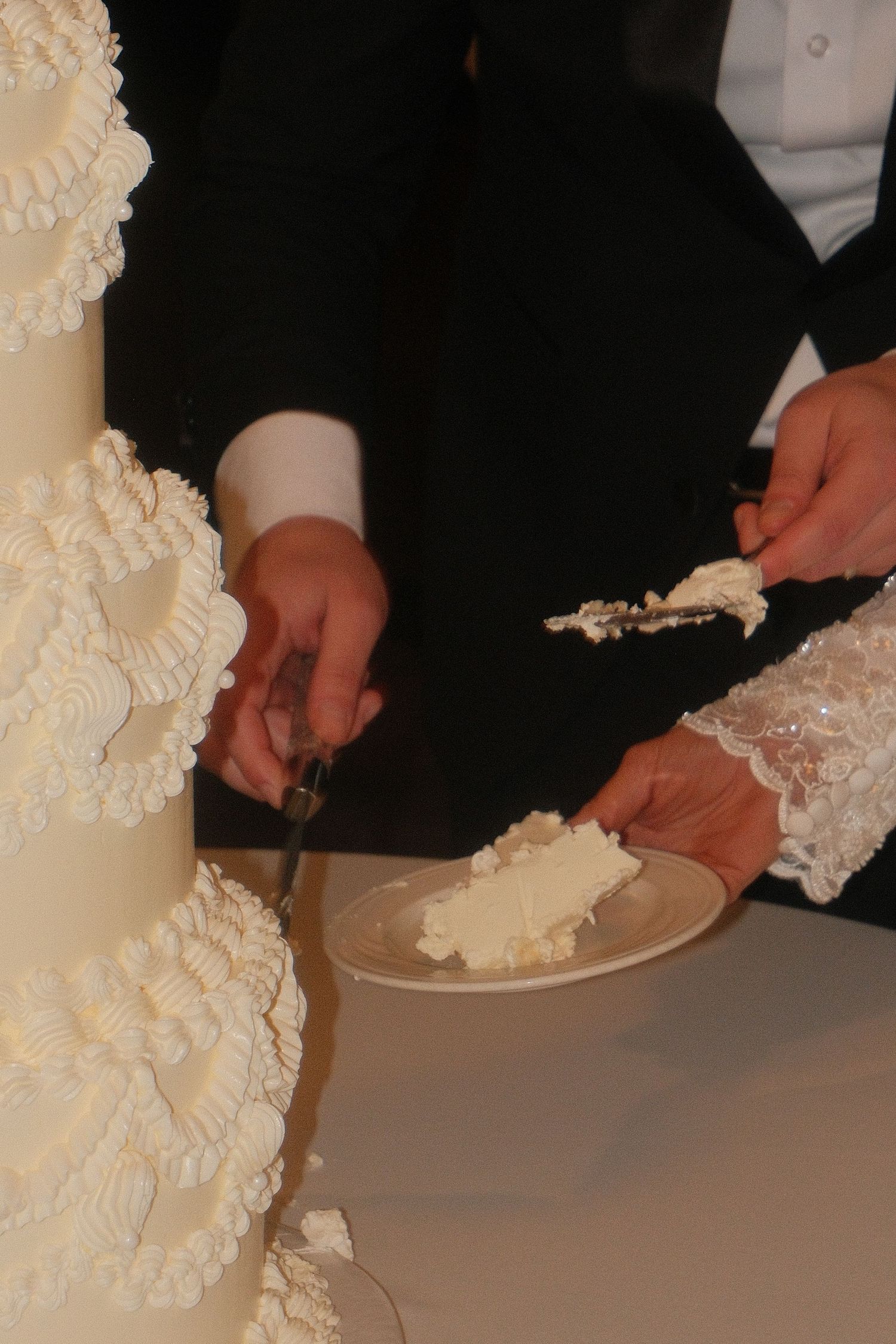 Bride and groom cutting elegant white multi-tiered wedding cake with lace decorations.