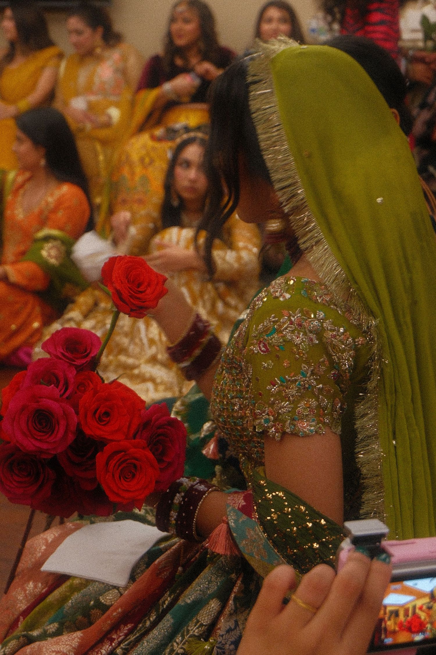 Bride in green embroidered lehenga holding red roses bouquet at a traditional South Asian wedding ceremony.