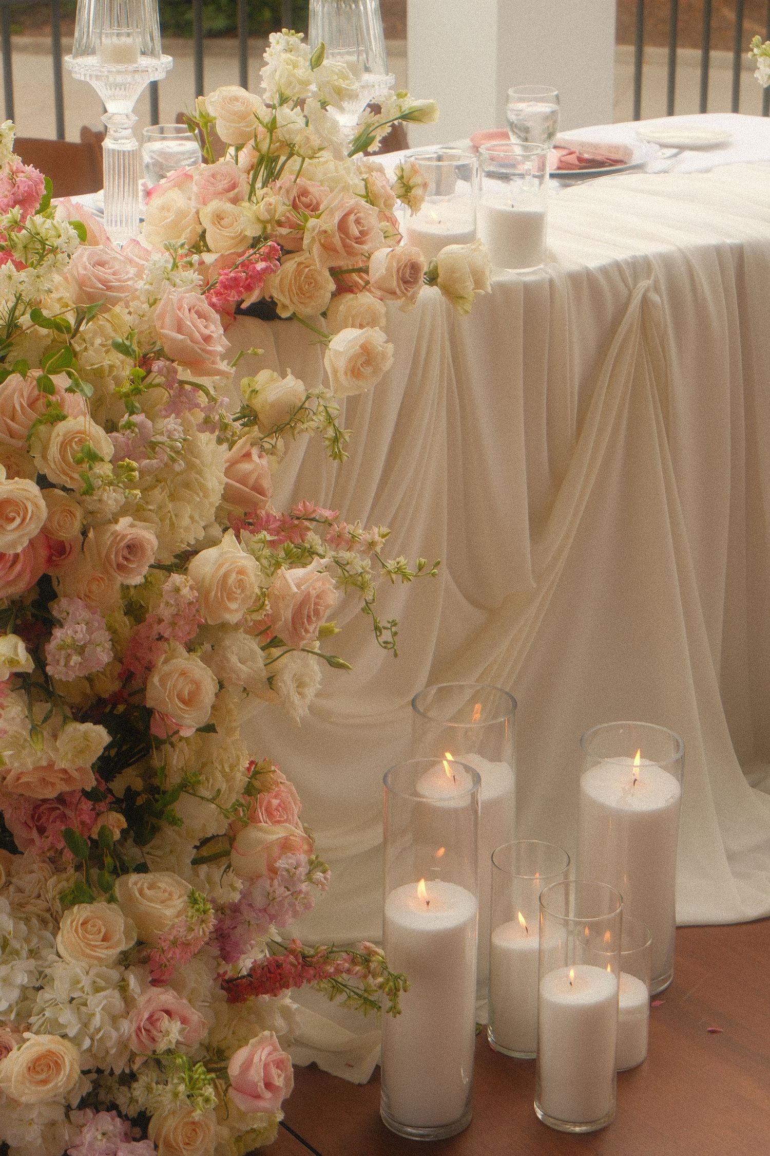 Wedding sweetheart table decorated with pink roses, white hydrangeas, and glowing pillar candles.