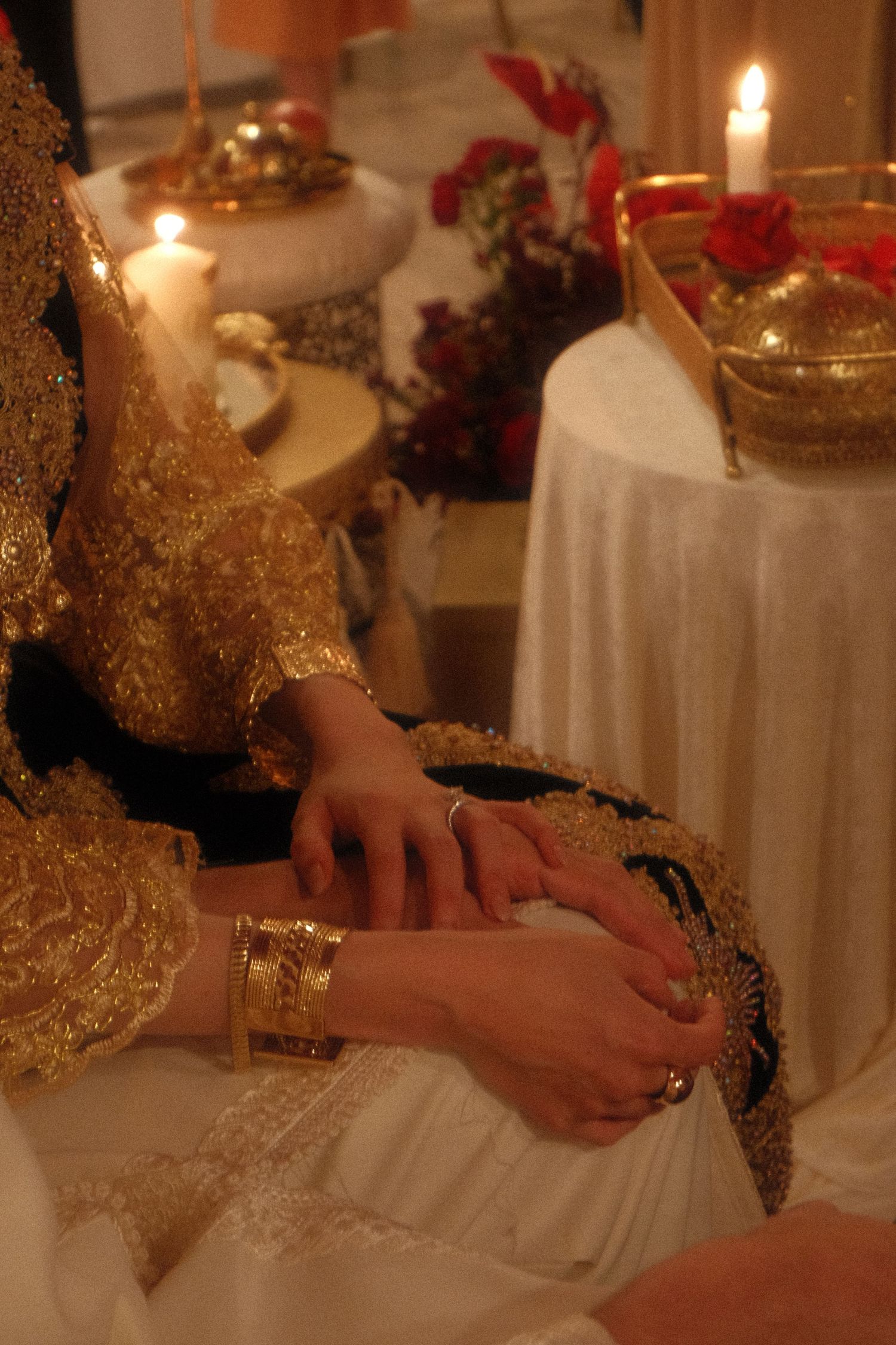 Bride in gold embroidered lehenga with gold bangles seated near candles during a South Asian wedding ritual.