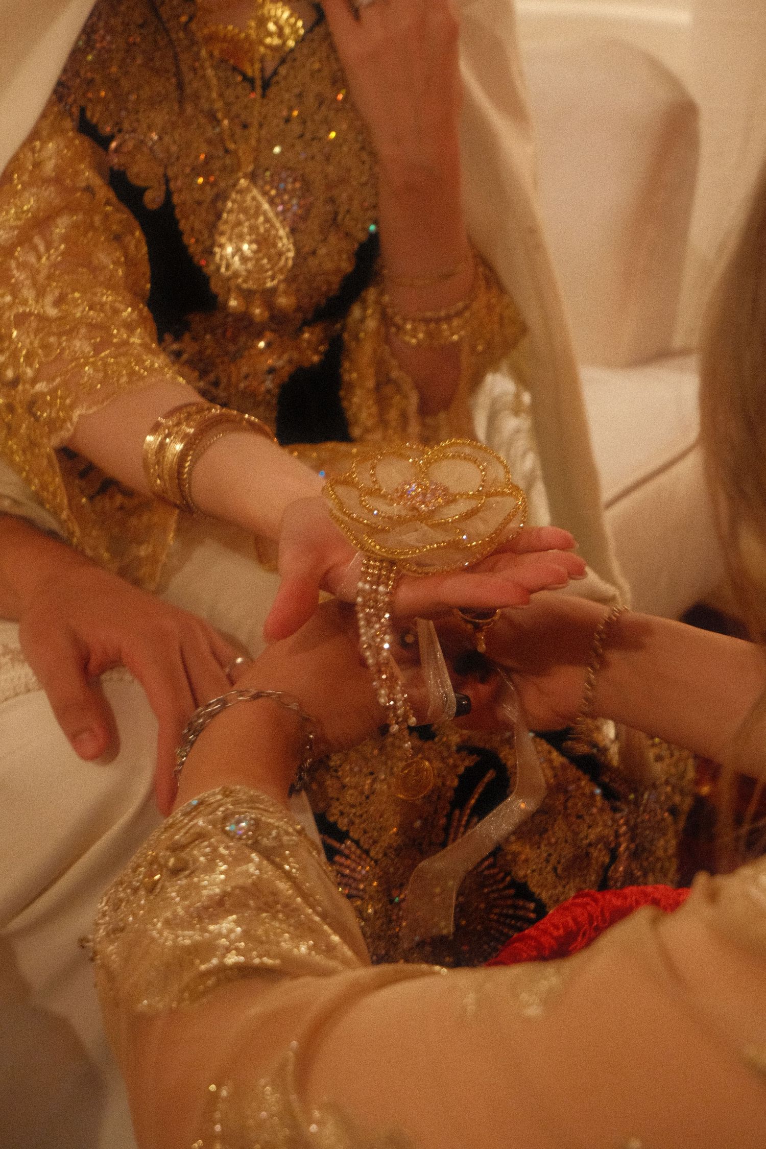 Hands adorned with gold jewelry and henna exchange ornate accessories during a traditional wedding ceremony.