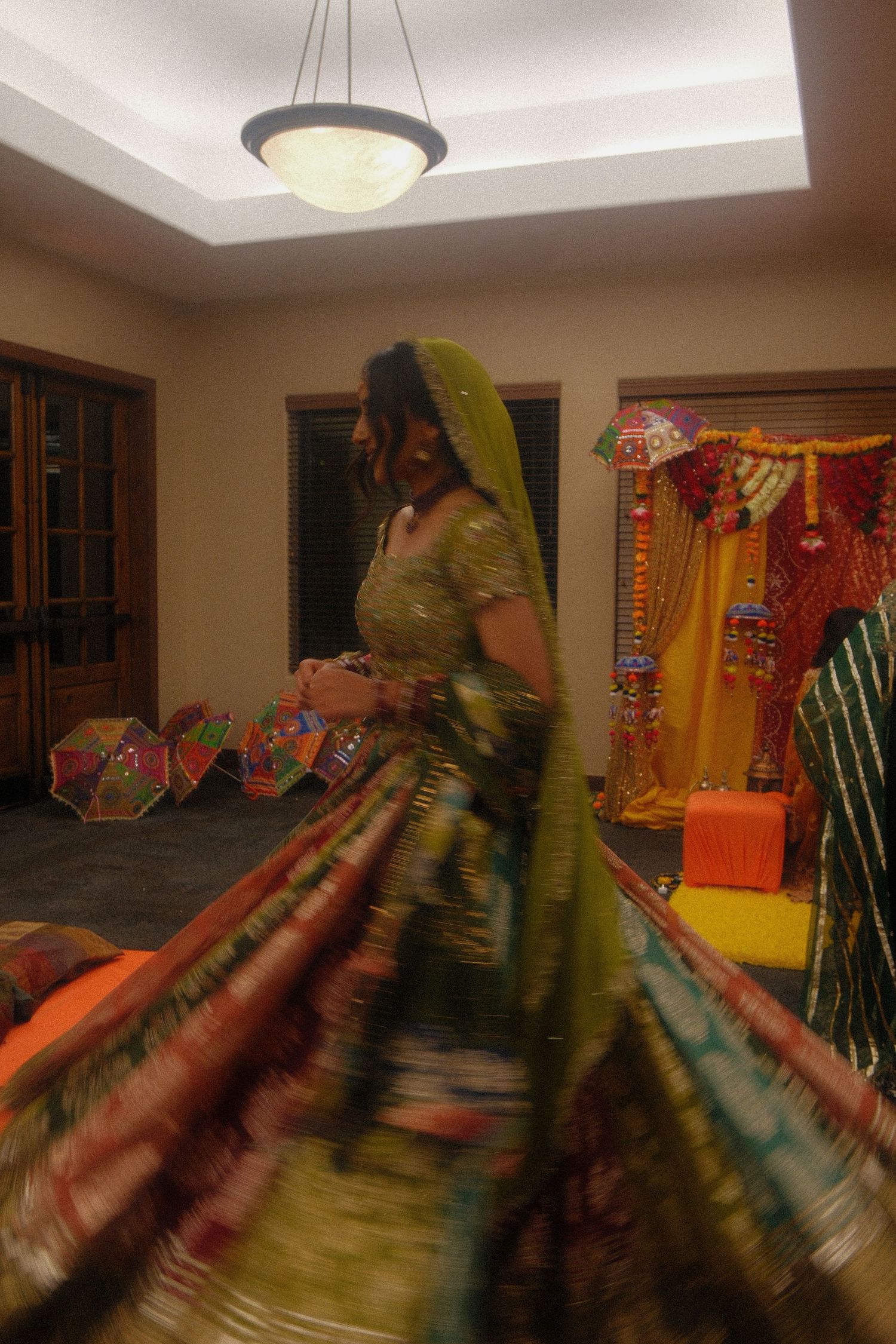 Bride twirling in a green and multicolor lehenga during a South Asian mehndi ceremony with colorful decorations.