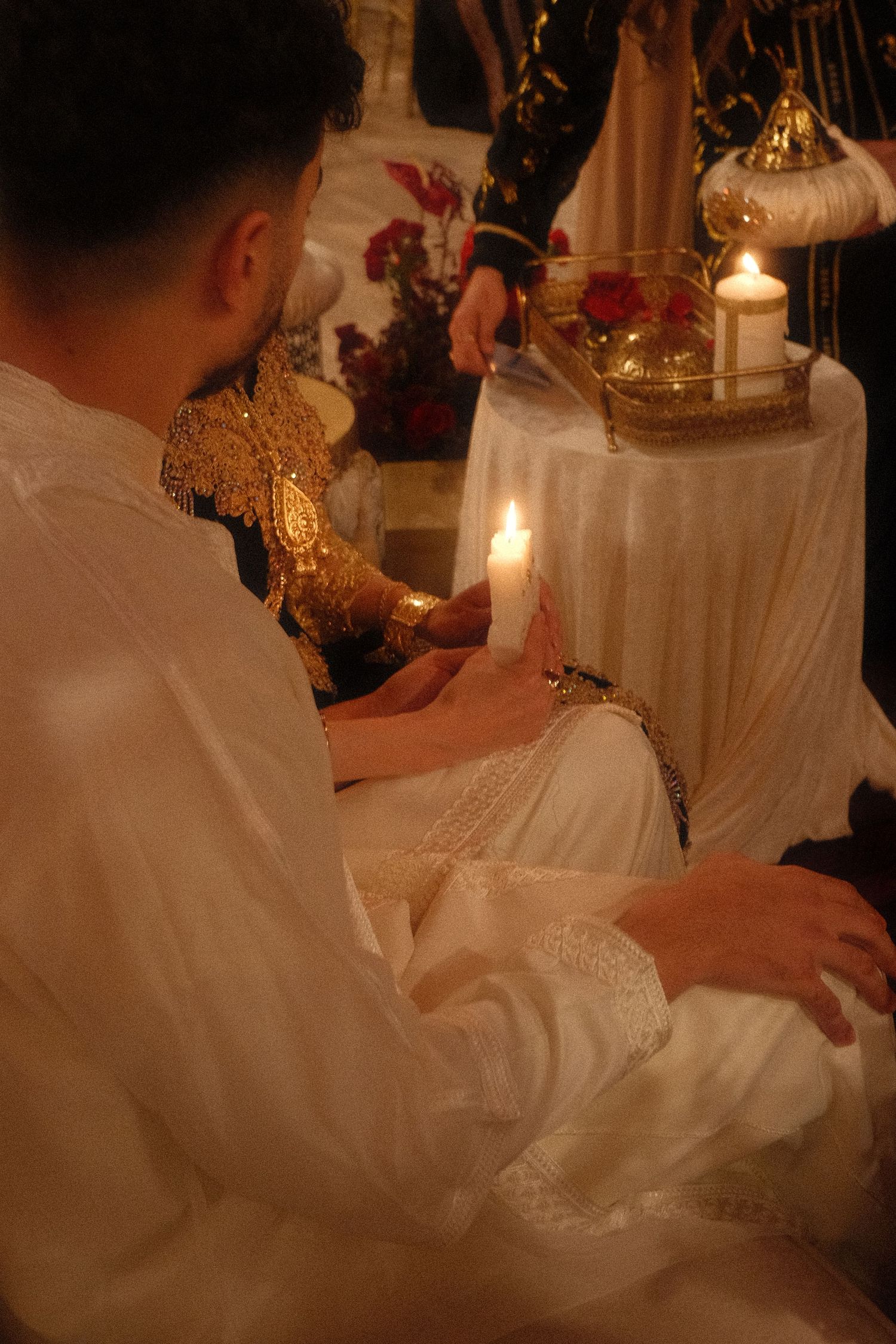 A groom in white traditional attire holds a lit candle during a ceremonial wedding ritual.
