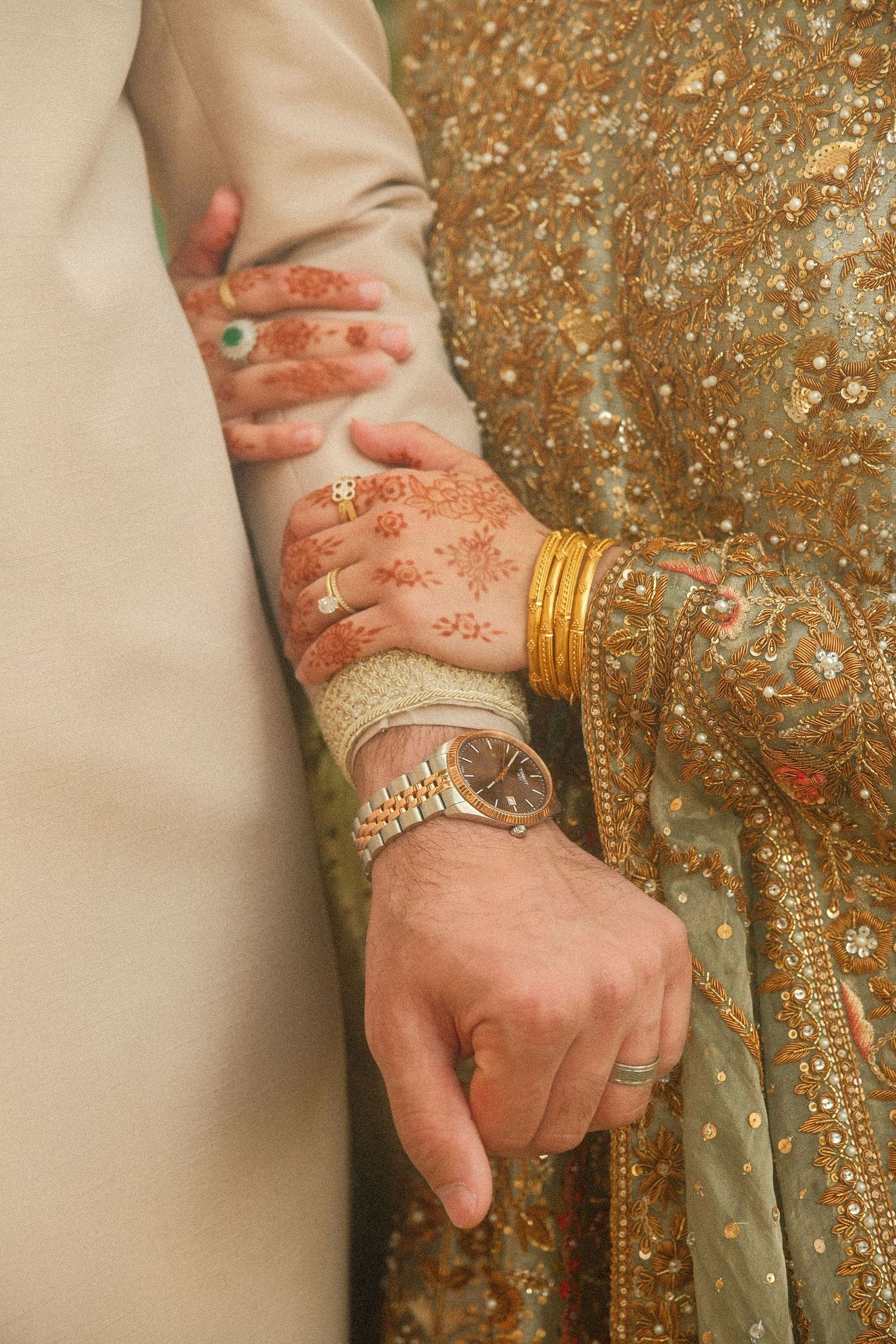 Close-up of bride and groom hands, bride with henna mehndi bangles holding grooms arm with watch.