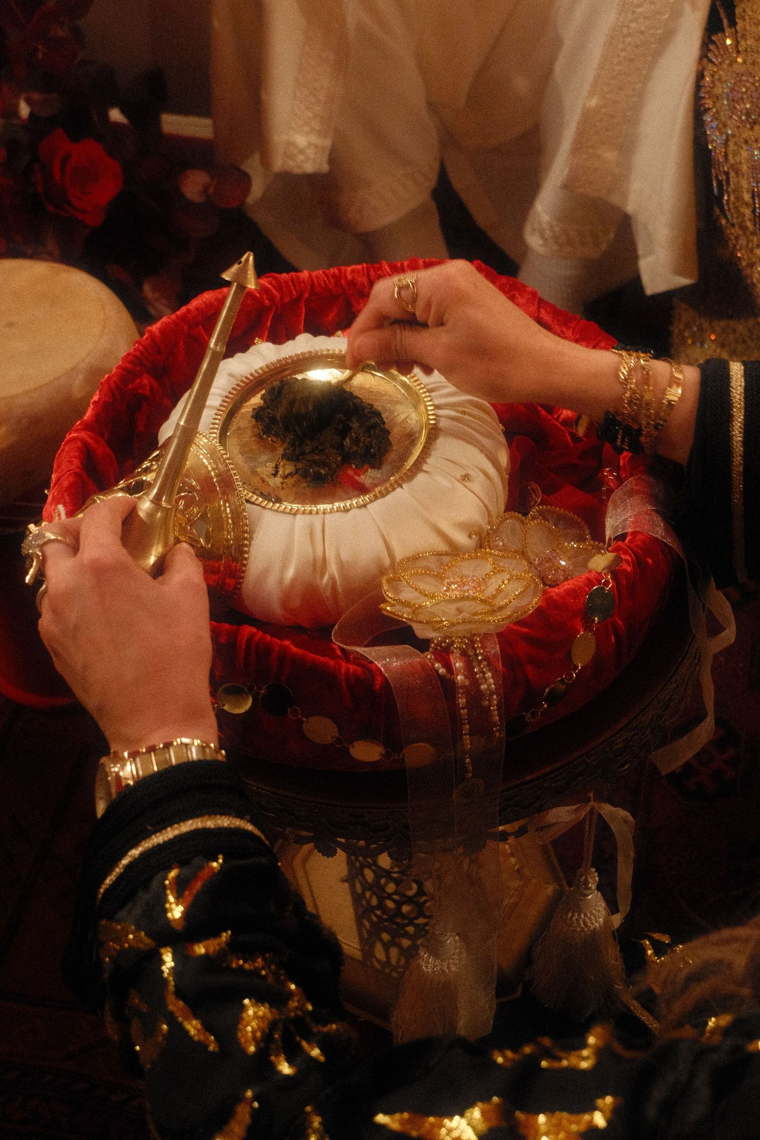 Hands with gold bangles holding a decorated ceremonial basket with gold items during a South Asian wedding ritual.