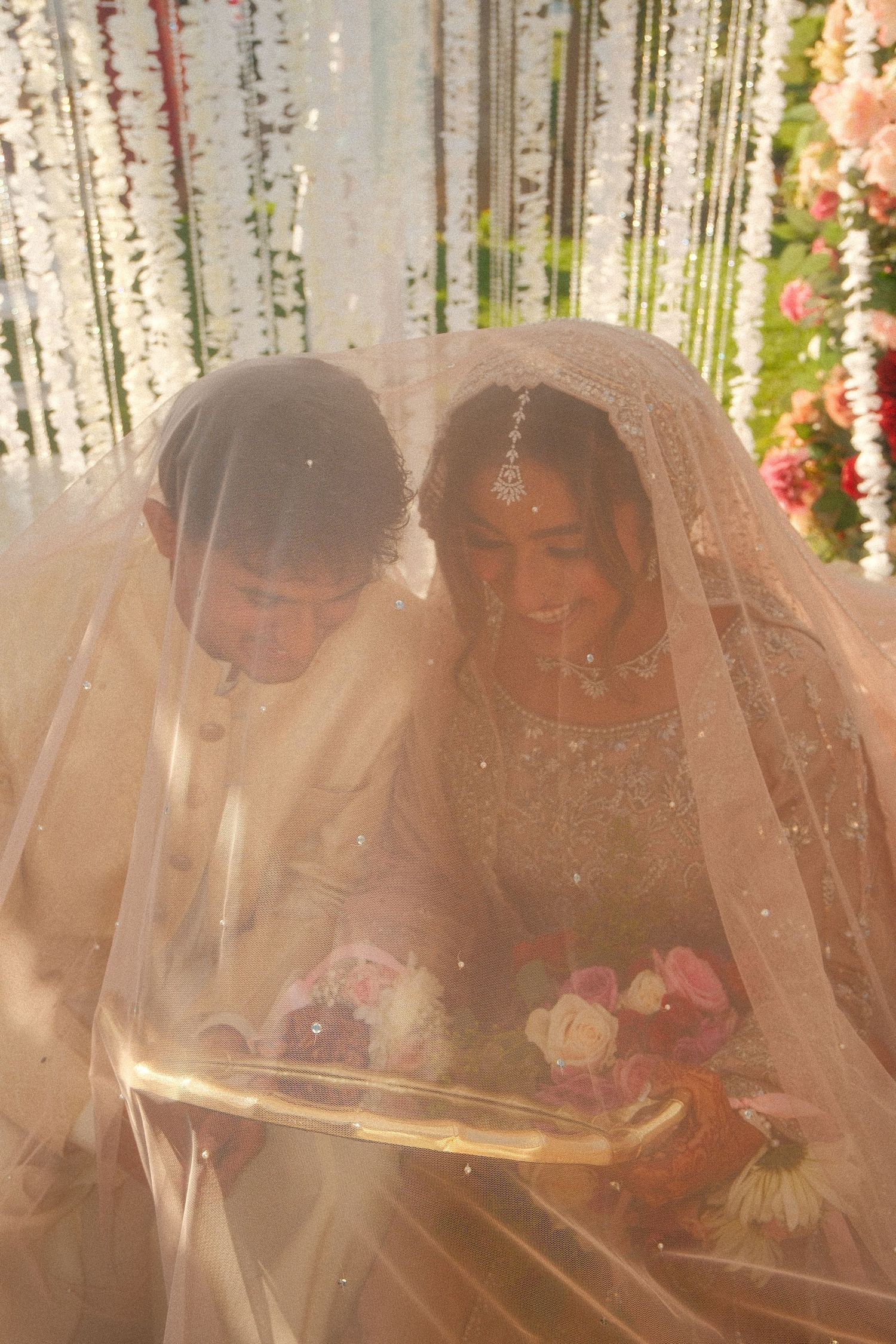 Muslim couple sharing intimate moment under wedding veil reading Quran at traditional nikah ceremony.