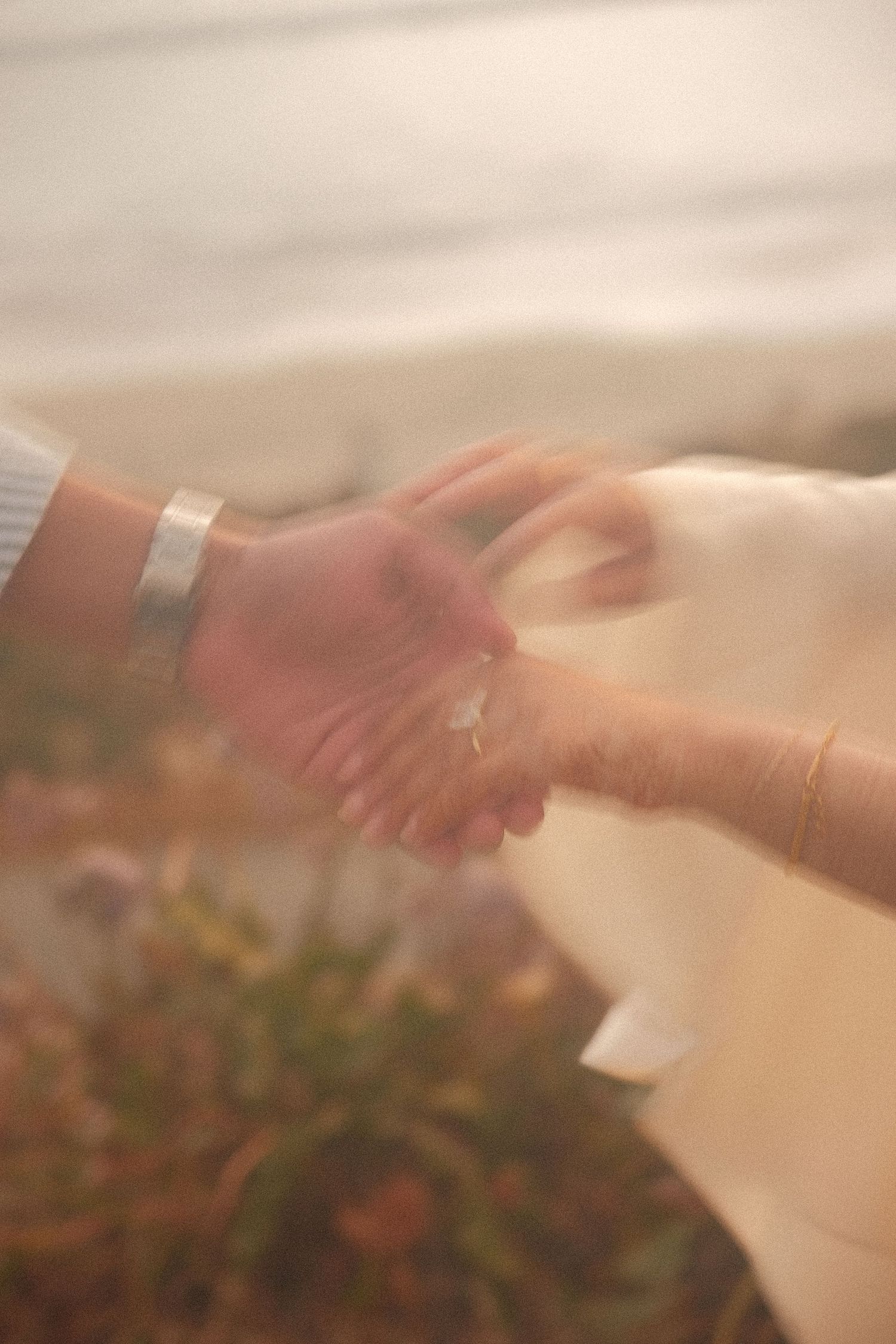 Couple clasping hands tenderly outdoors, woman wearing delicate gold bracelet and engagement ring.