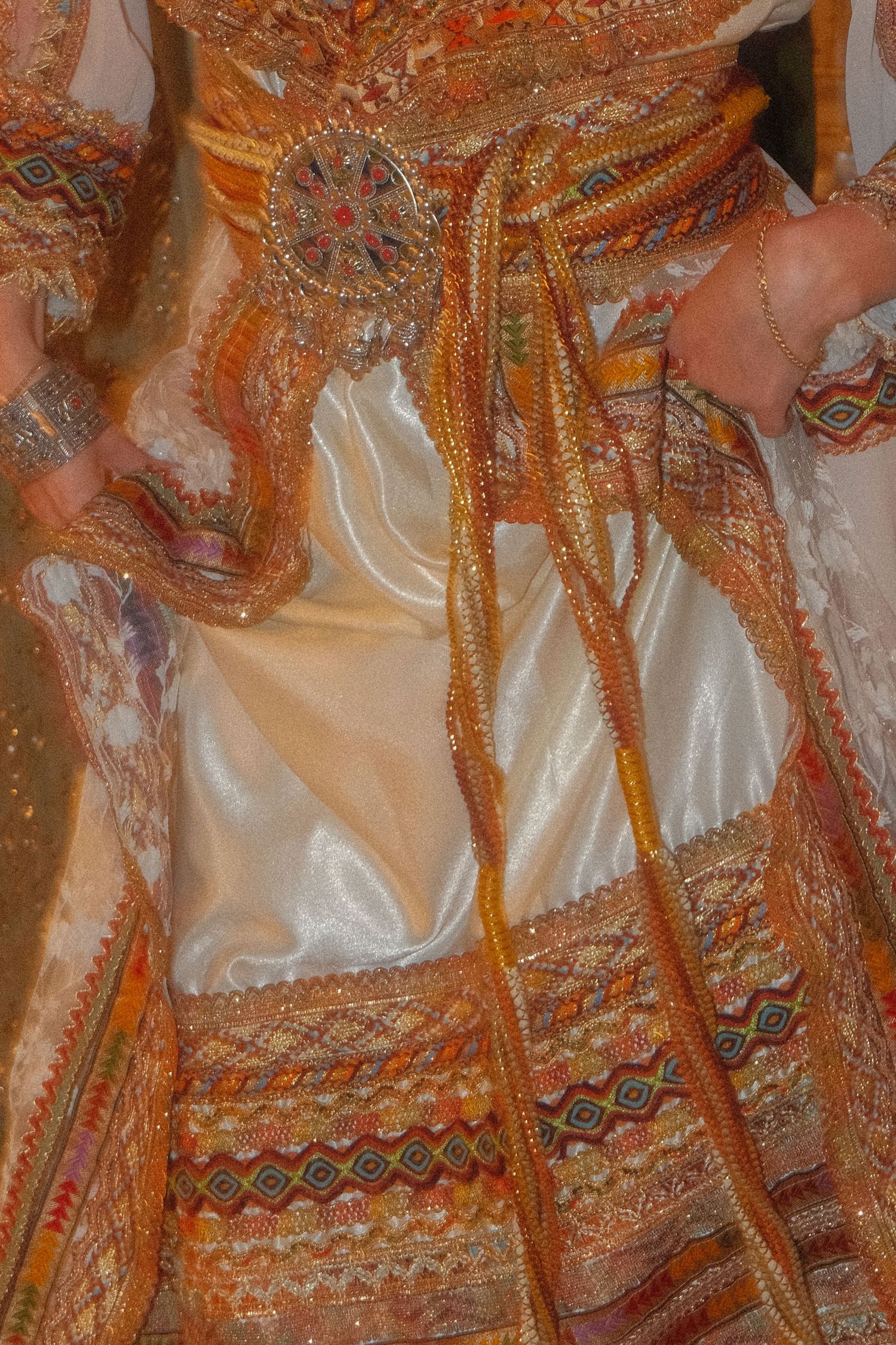 Close-up of an ornate traditional wedding dress with gold embroidery, colorful trim, and decorative belt.