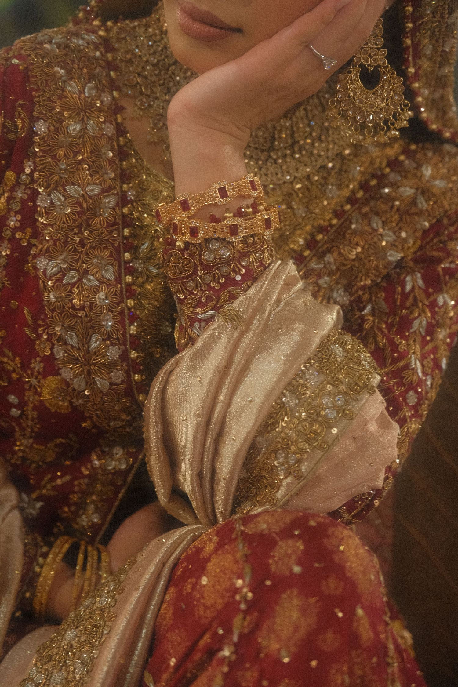 Close-up of bride in ornate red and gold Pakistani bridal outfit with gold jewelry and bangles.