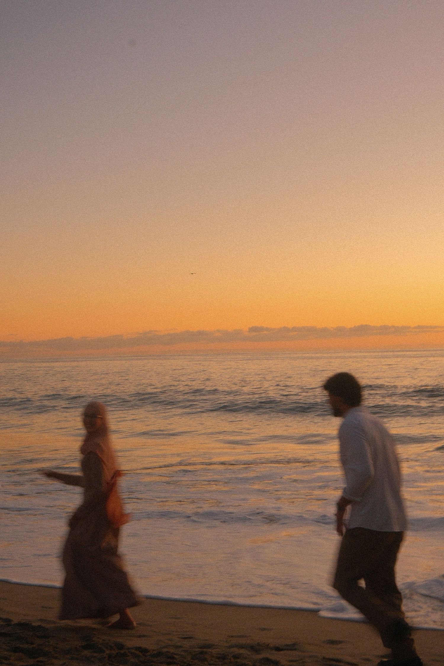 Couple walking on beach at golden sunset, blurred motion photography.