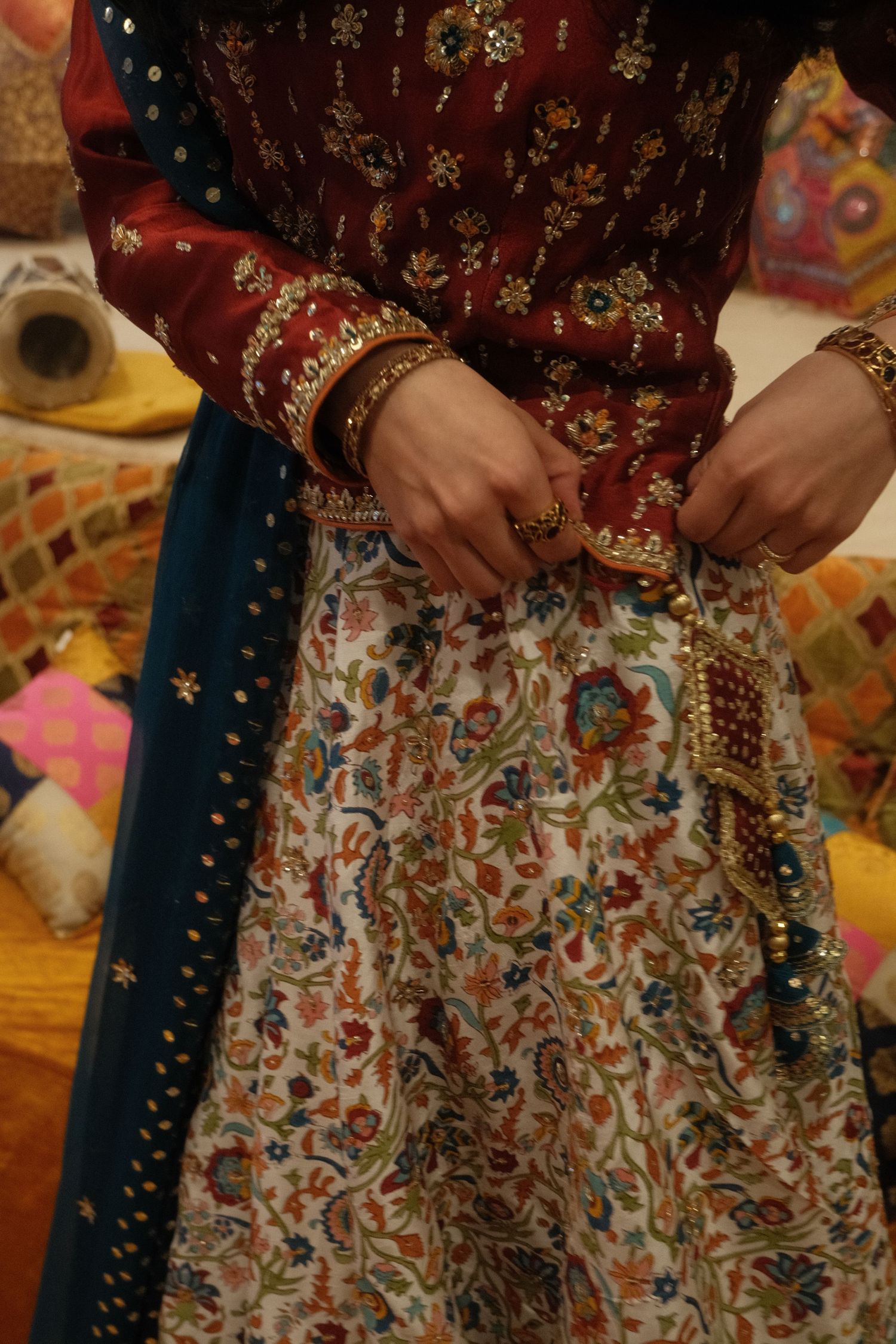 Close-up of a bride in a maroon embroidered kurta and white floral lehenga adorned with gold bangles and rings.