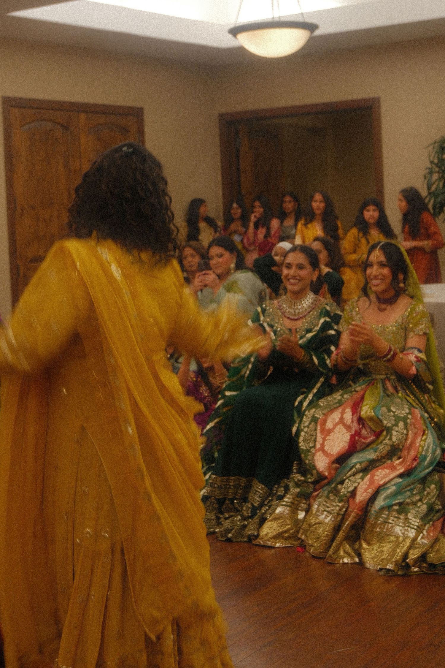 Woman in yellow salwar dancing at a South Asian wedding celebration with guests in traditional attire watching.