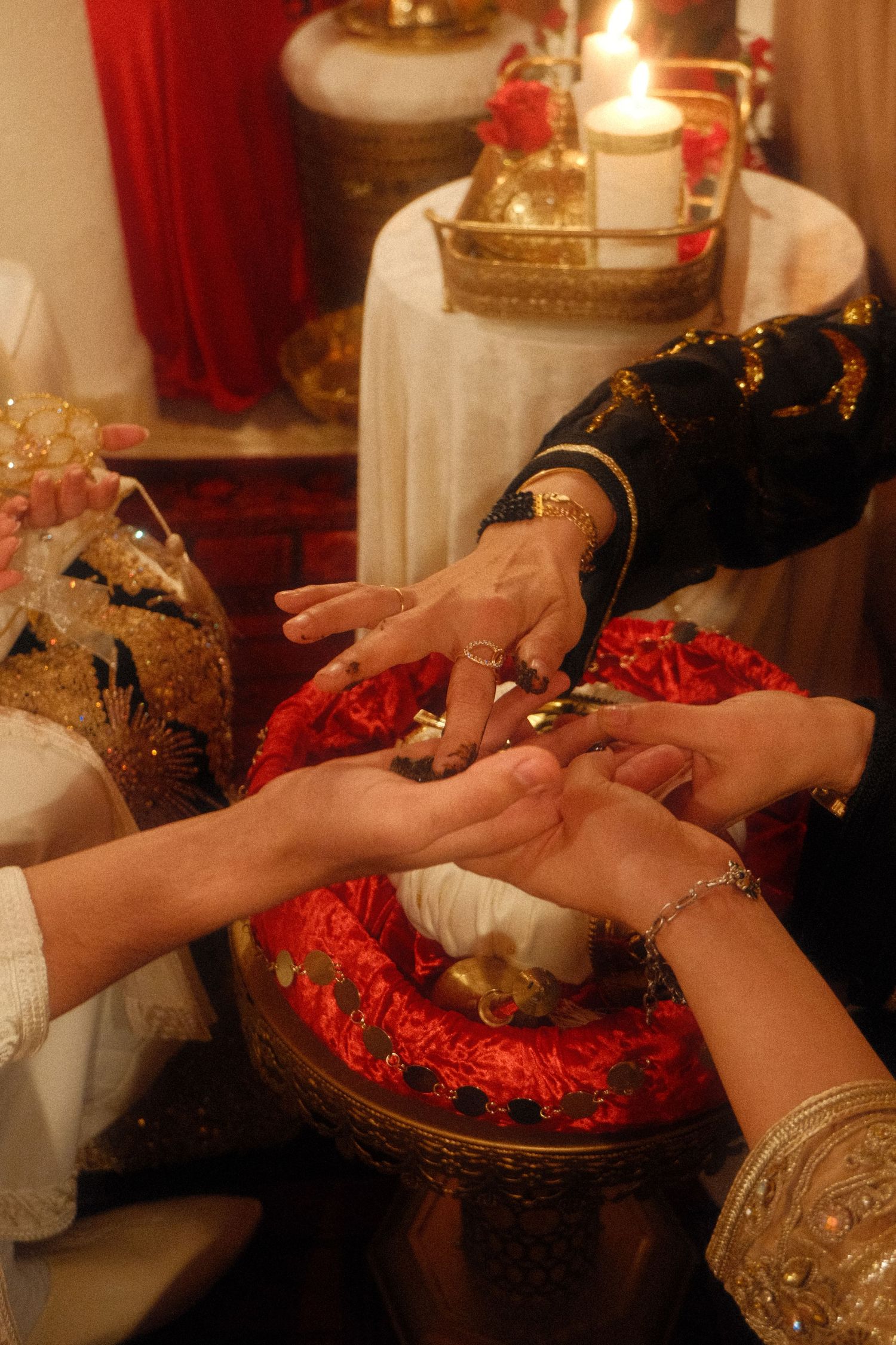 Multiple hands exchange gold rings over a red cushion during a traditional wedding ring ceremony.