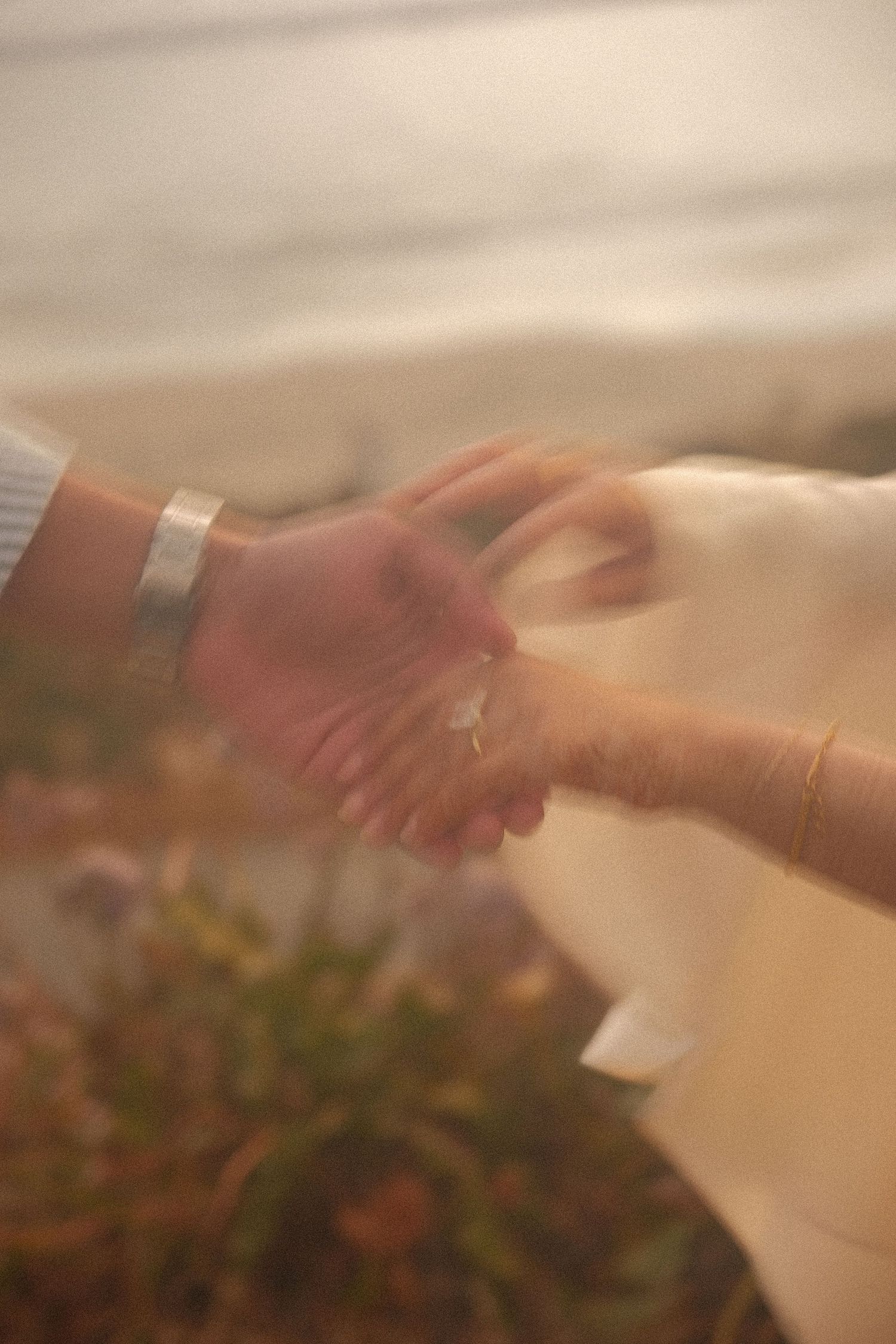 Close-up of a couple holding hands near the water, woman wearing a diamond ring and gold bracelet.