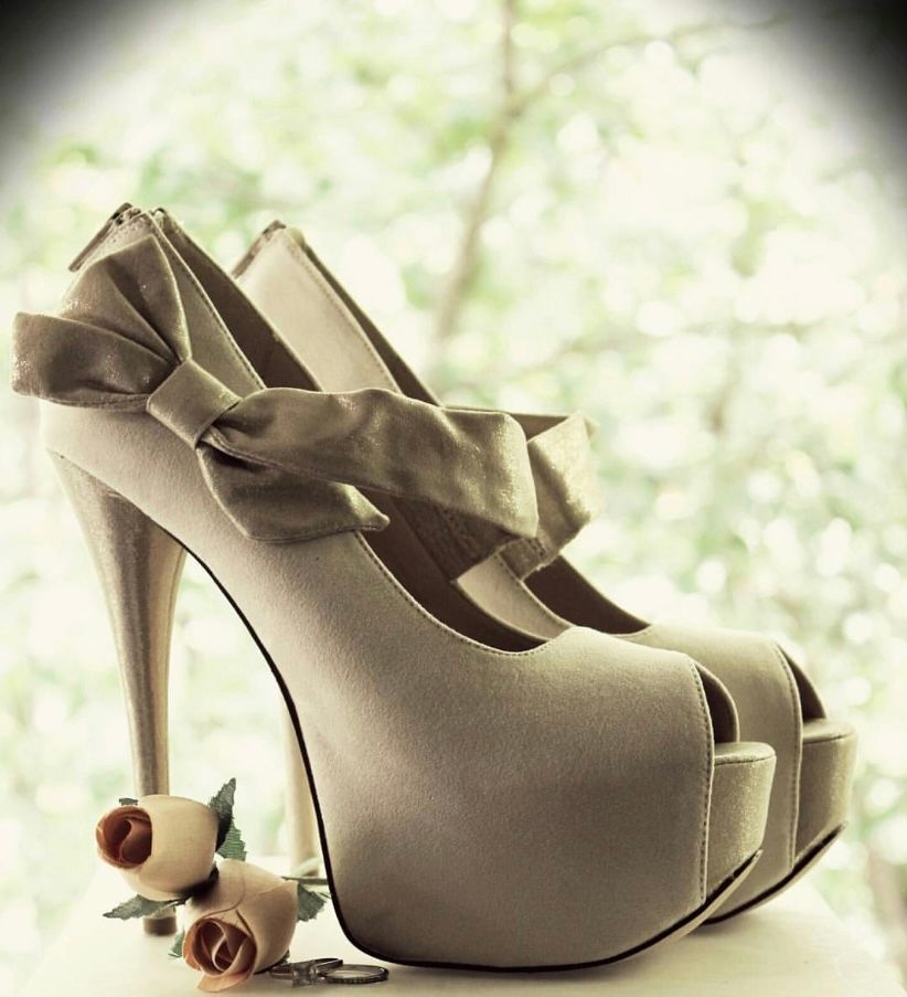 Elegant ivory bridal high heel shoes with satin bow and delicate rose details on soft bokeh background.