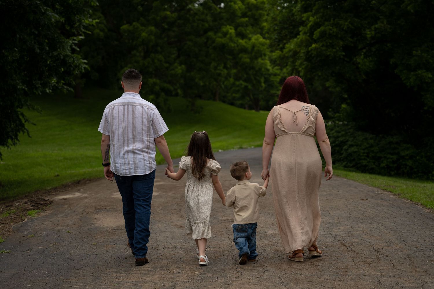 portrait of Family of four walking hand-in-hand along a tree-lined path in a lush green park.
