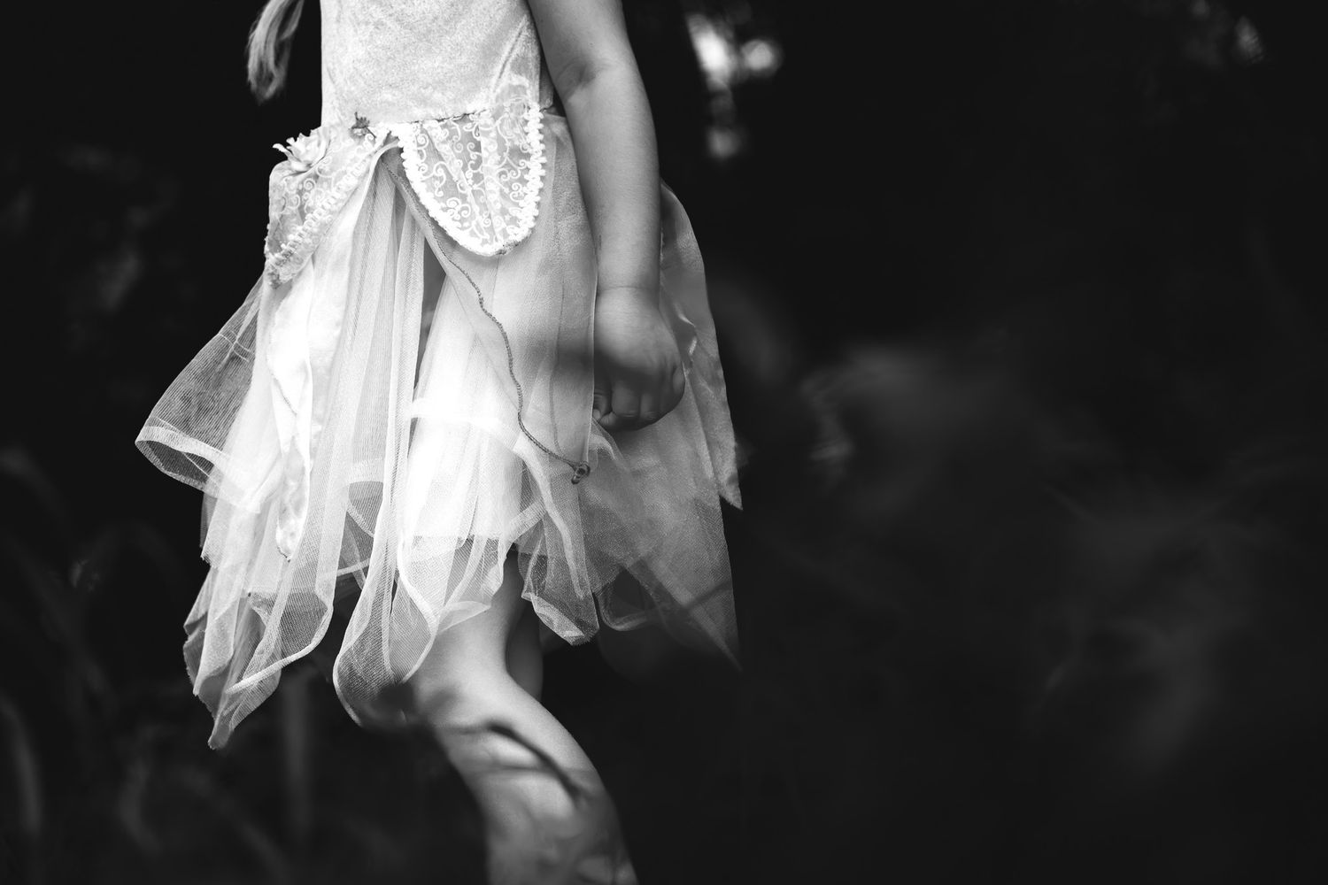 Black and white photo of a young girl in a white tulle fairy dress, captured from waist down outdoors. faceless family photography