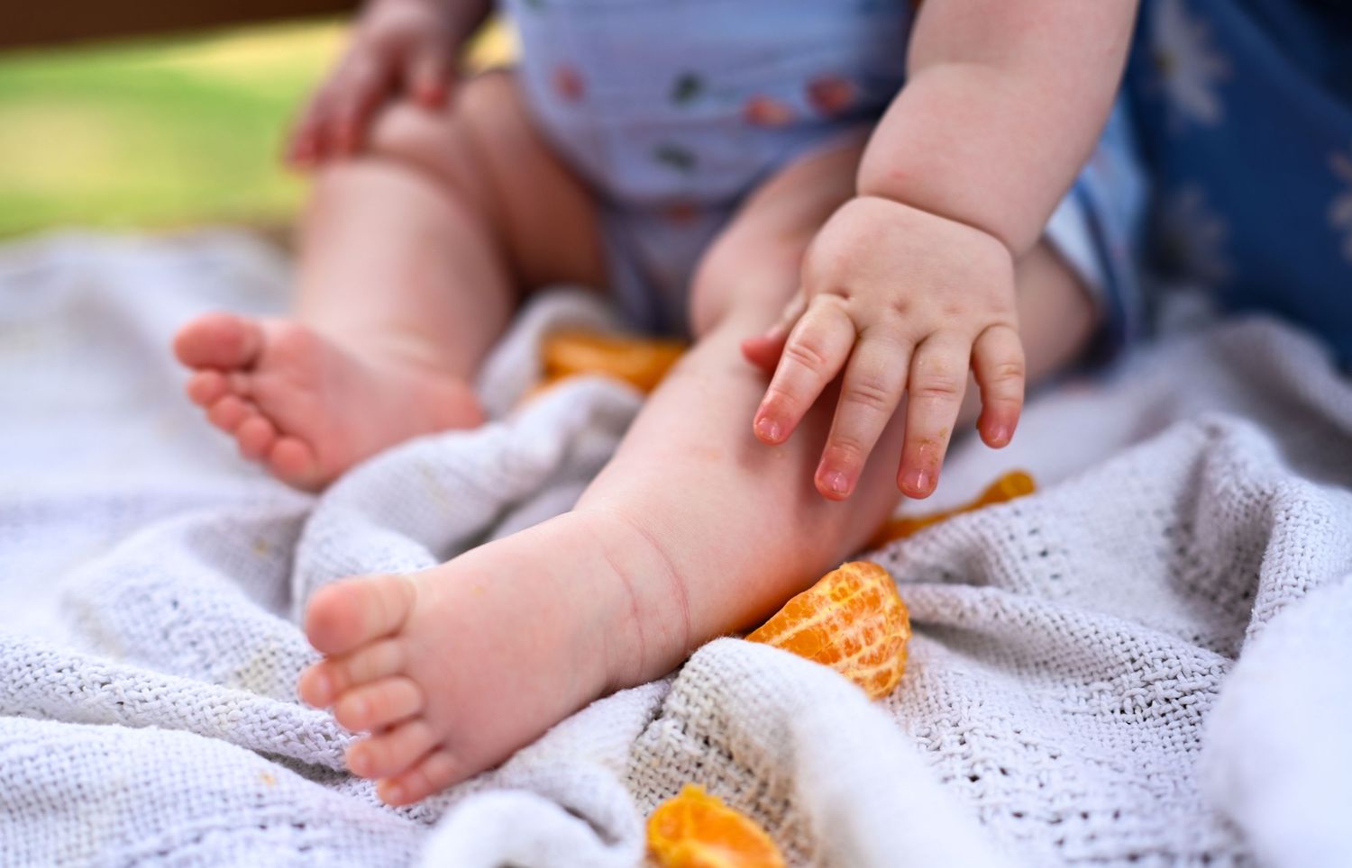 Close-up of baby feet and hands resting on a soft white blanket outdoors.
