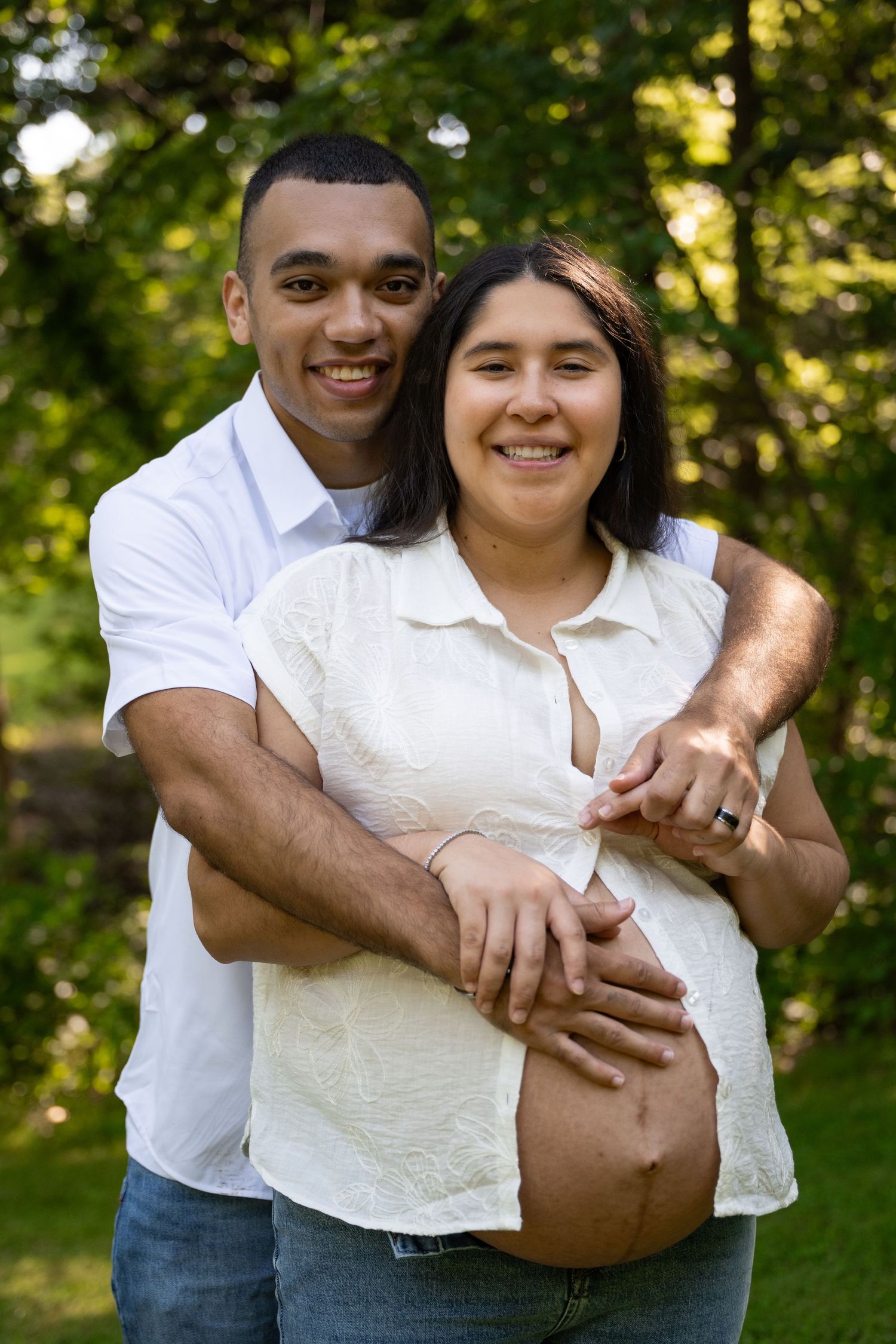 portrait of a Smiling expectant couple posing together outdoors, hands on pregnant belly in a green park.