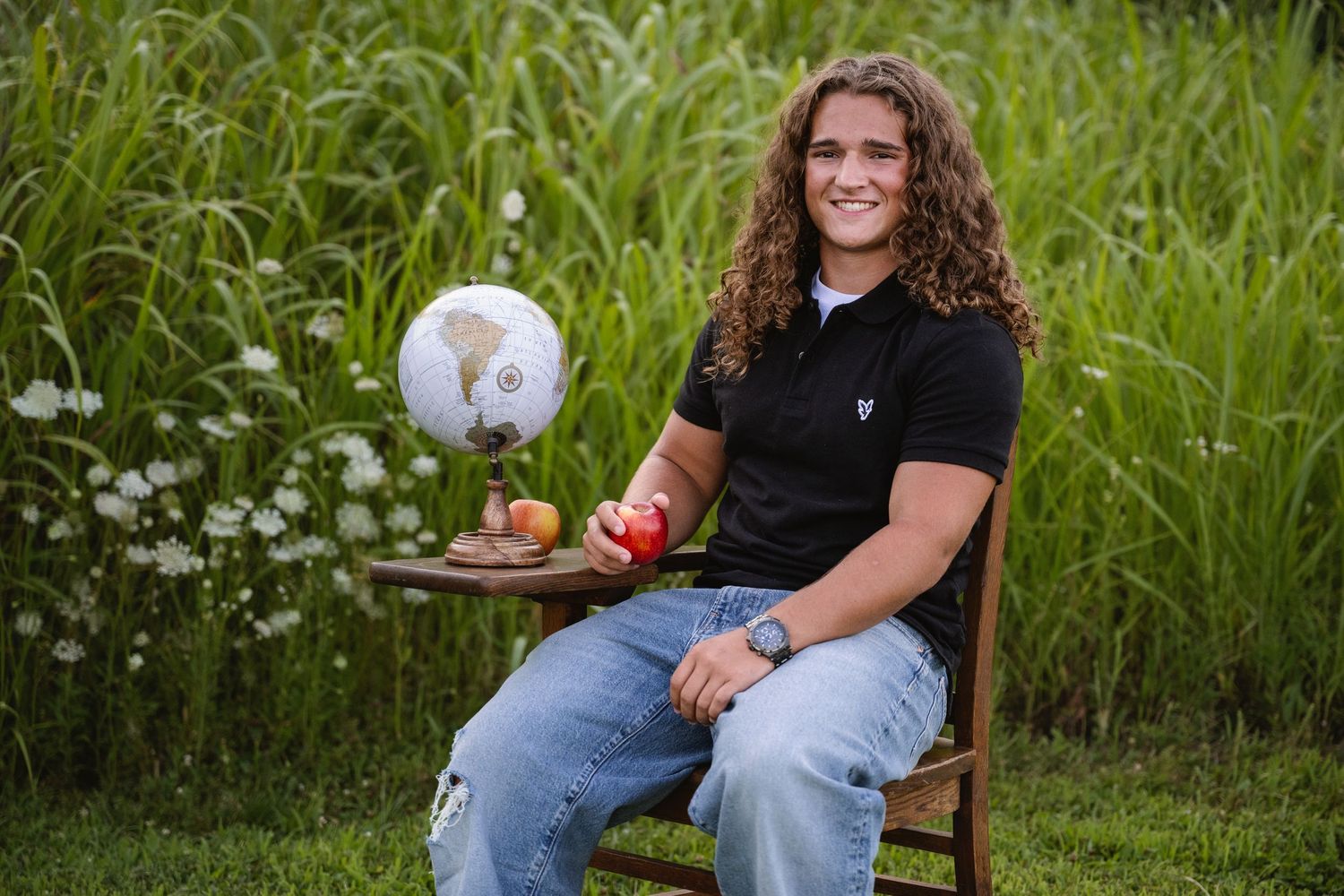 portrait of a Smiling young man with curly hair poses with globe and apple outdoors.