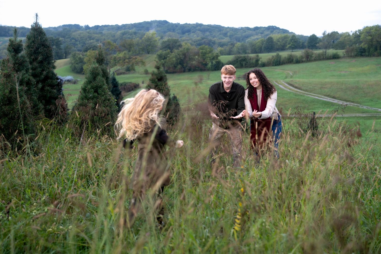 Three people in a lush green meadow with rolling hills and trees in background.