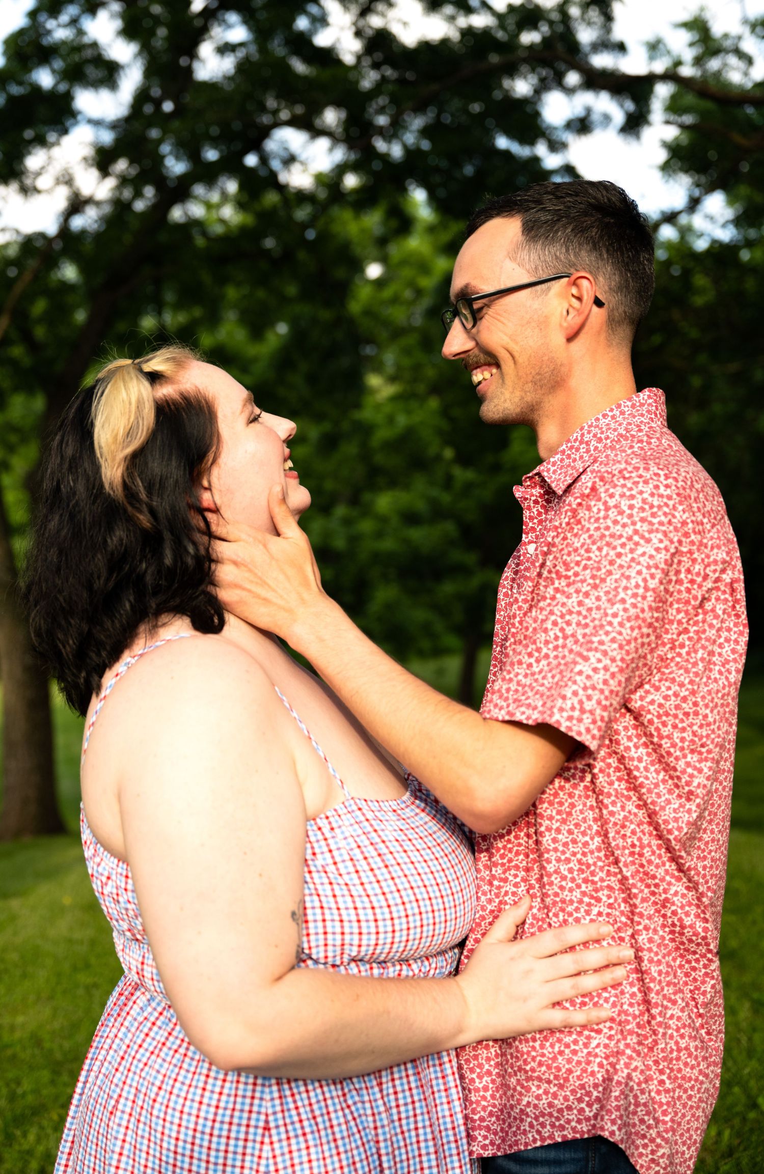 portrait of a Happy couple laughs and embraces in a green park, woman touching mans face tenderly.