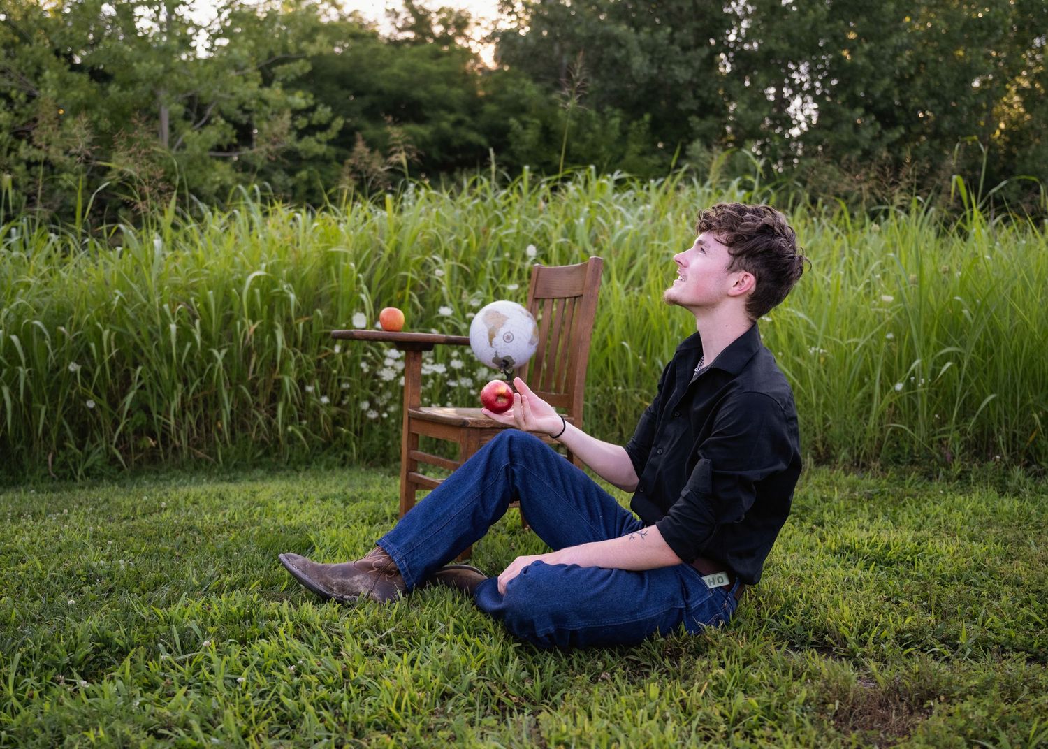 portrait of a Young man sitting in grass outdoors holding an apple with globe  behind him.