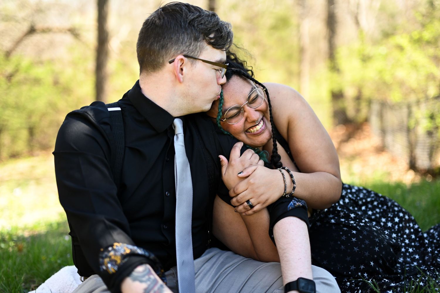 Happy interracial couple laughing and sitting together on green grass in a park.