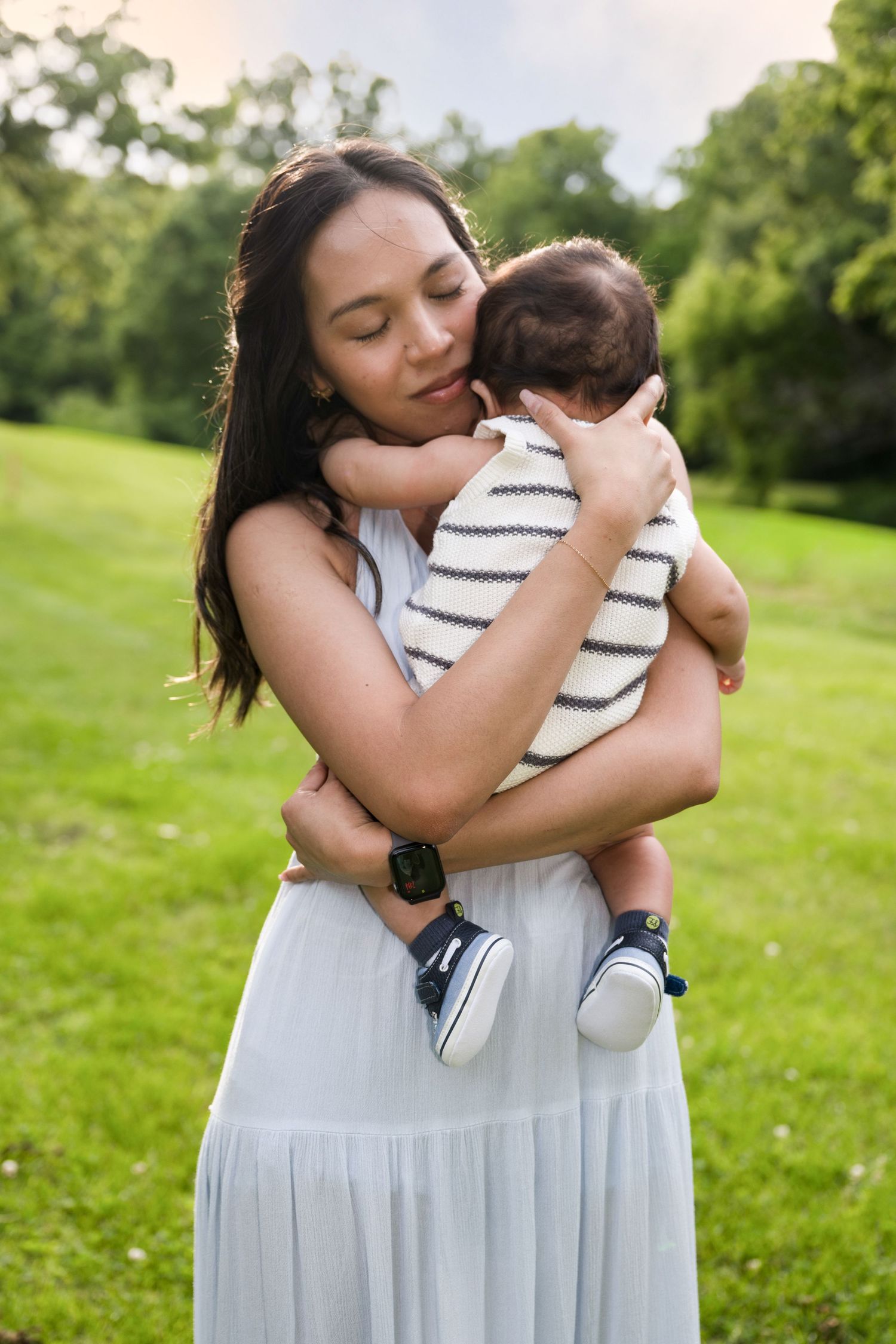 portrait of a Tender moment of a mother in white dress gently cradling her newborn baby in a lush green park.
