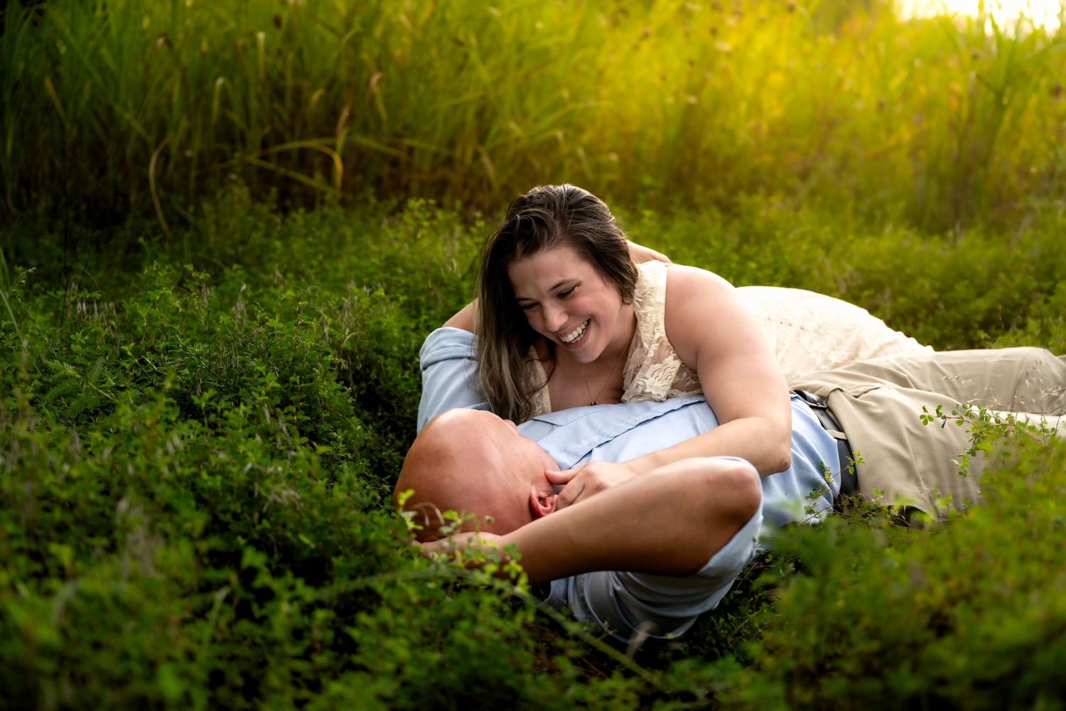lifestyle portrait of a Couple laughing and cuddling in lush green field during golden hour