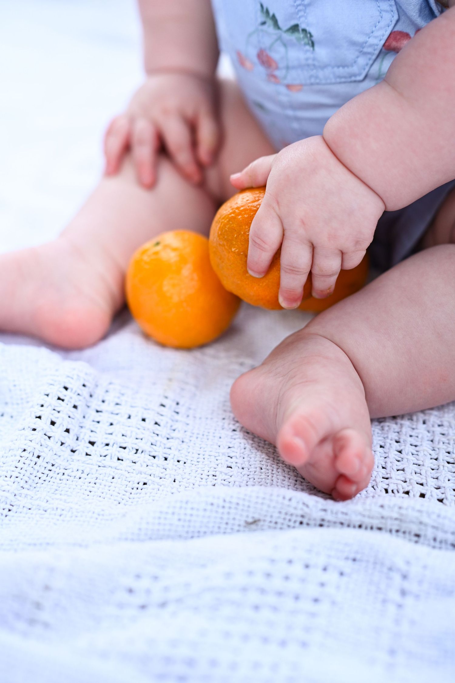 Baby hands and feet with two fresh oranges on a white knit blanket.
