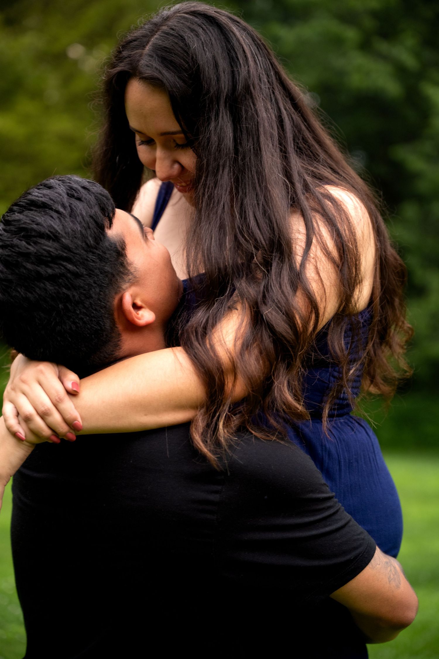 lifestyle portrait of a couple sharing a romantic moment outdoors, with the man lifting the woman as they lean in for a kiss.