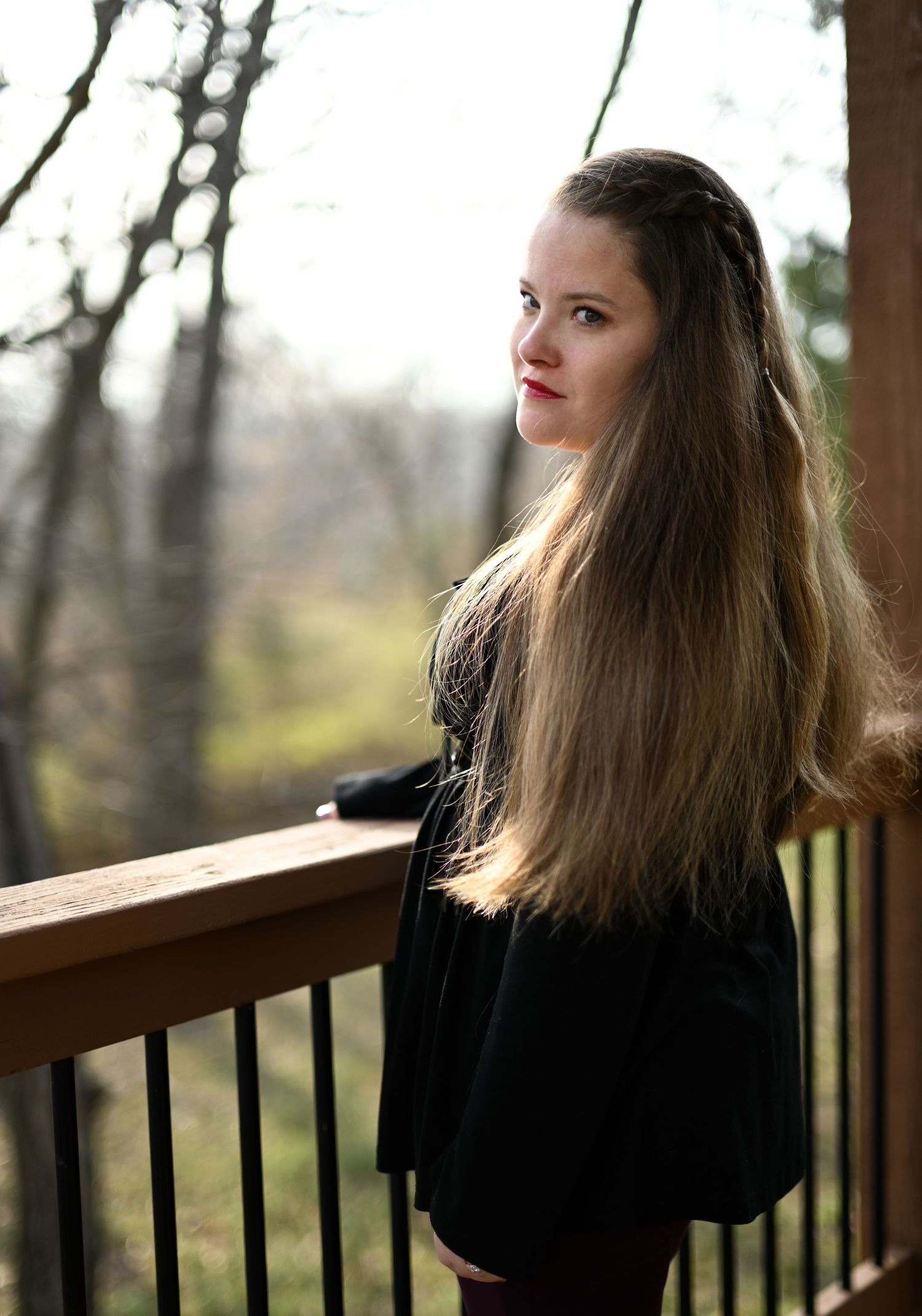 Young woman with long flowing hair in black outfit posing on wooden deck in nature.