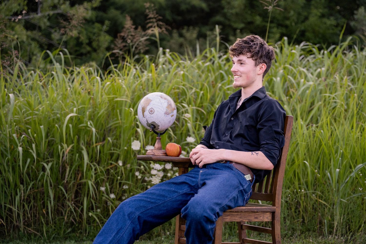 portrait of a Smiling teenage boy in black shirt and jeans sitting outdoors with globe.