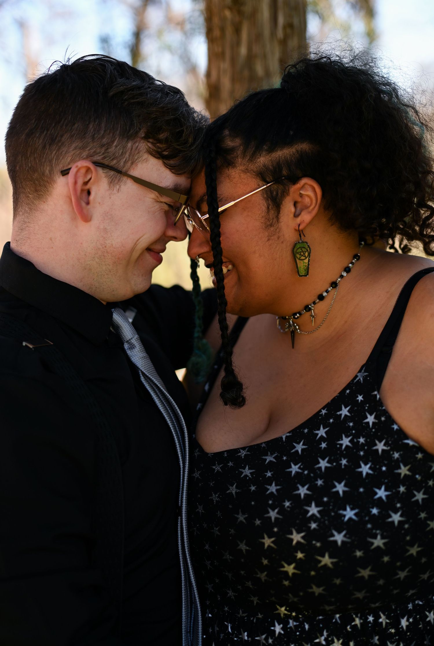 Smiling interracial couple touching foreheads tenderly outdoors in warm sunlight.
