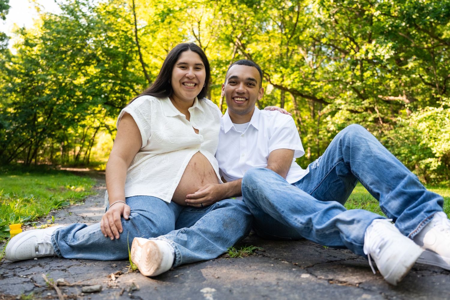 portrait of a Happy expectant couple sitting together in a sunny green park, smiling warmly.