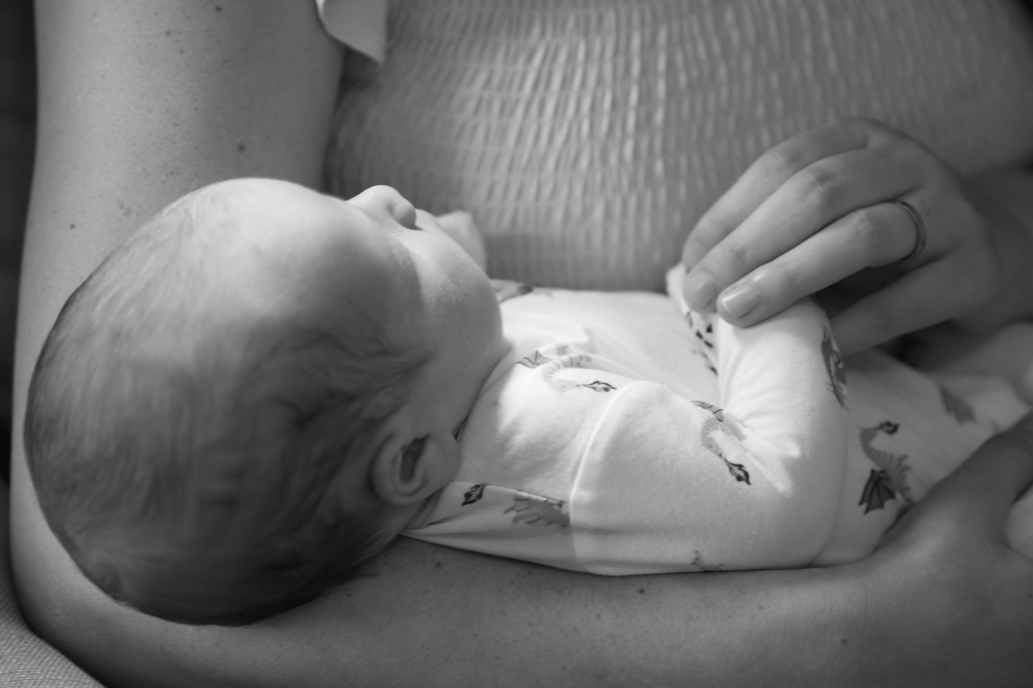 Black and white photo of a newborn baby cradled in mother's arms, looking up peacefully.