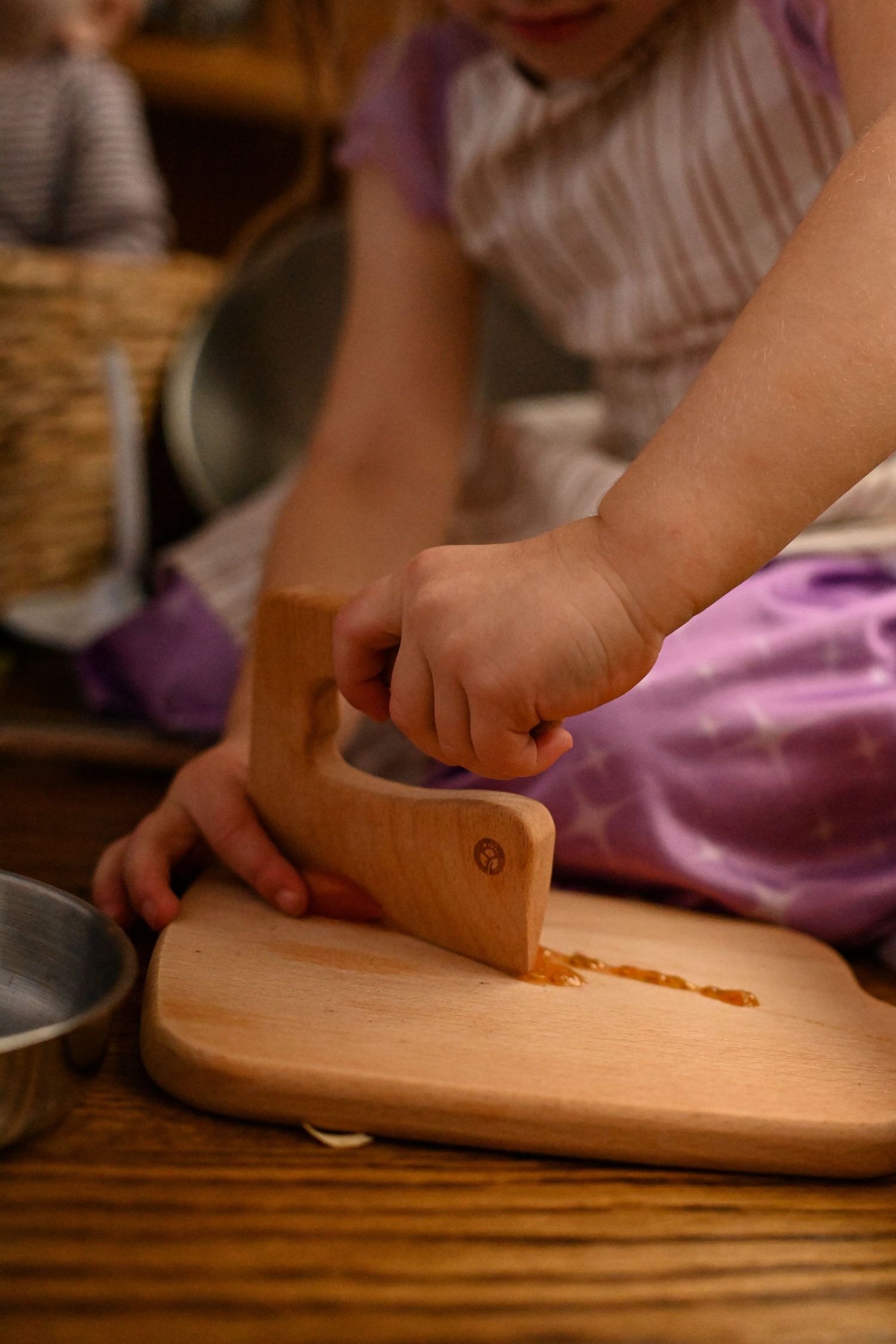 Young child using a wooden pastry cutter on a wooden cutting board.