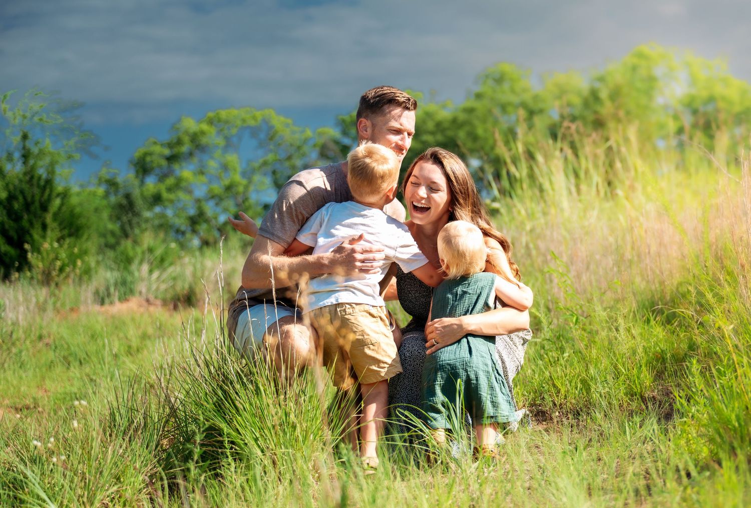 Happy family with two young children embracing in a lush green meadow on a sunny day.