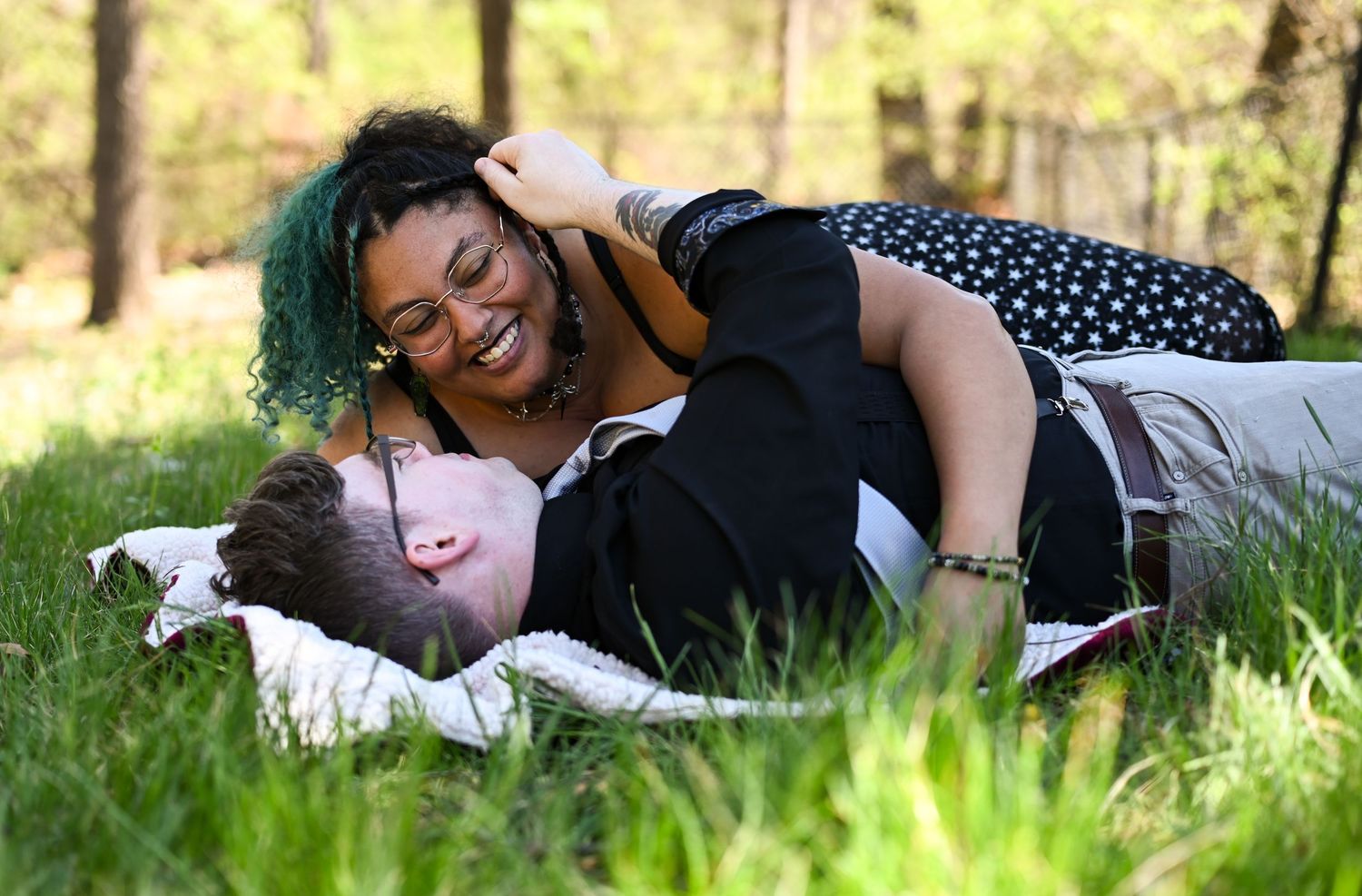 Joyful woman with green hair lying on a man in the grass laughing outdoors.