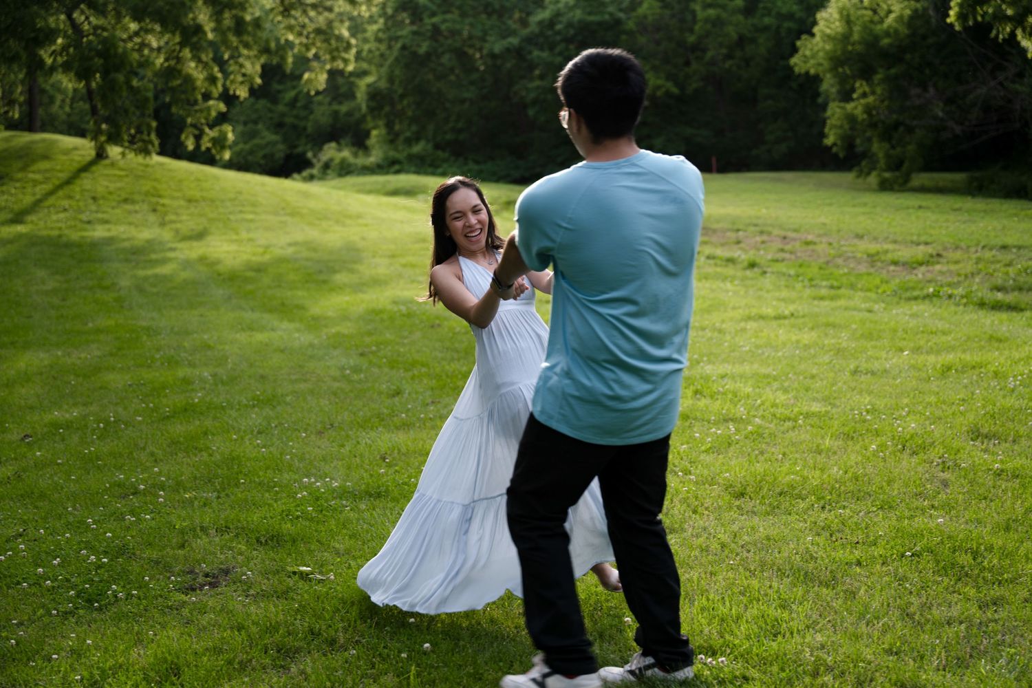 portrait of a Couple dances and spins joyfully on a wide green lawn at dusk in a park.