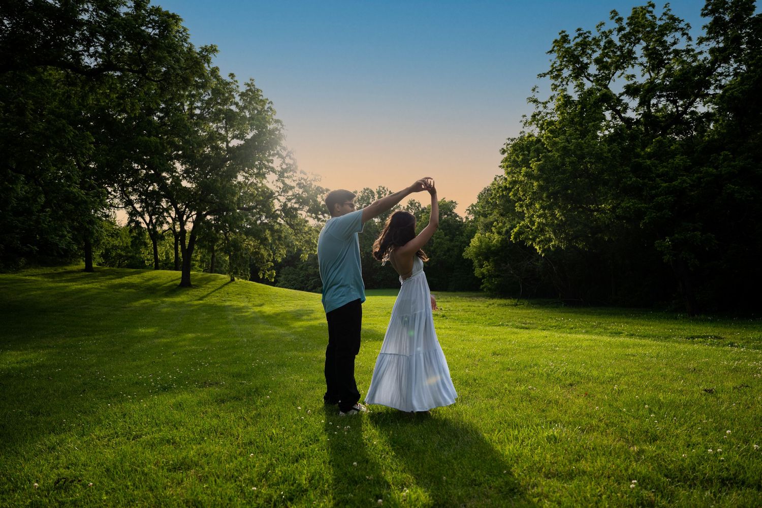 portrait of a Couple dances under arching trees at golden sunset on a vibrant green lawn.