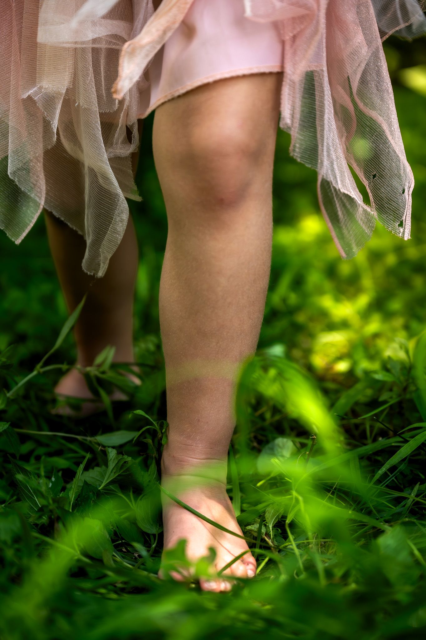 Child's bare feet on green grass wearing a pink tutu skirt outdoors in nature. faceless family photography in Leavenworth, KS.