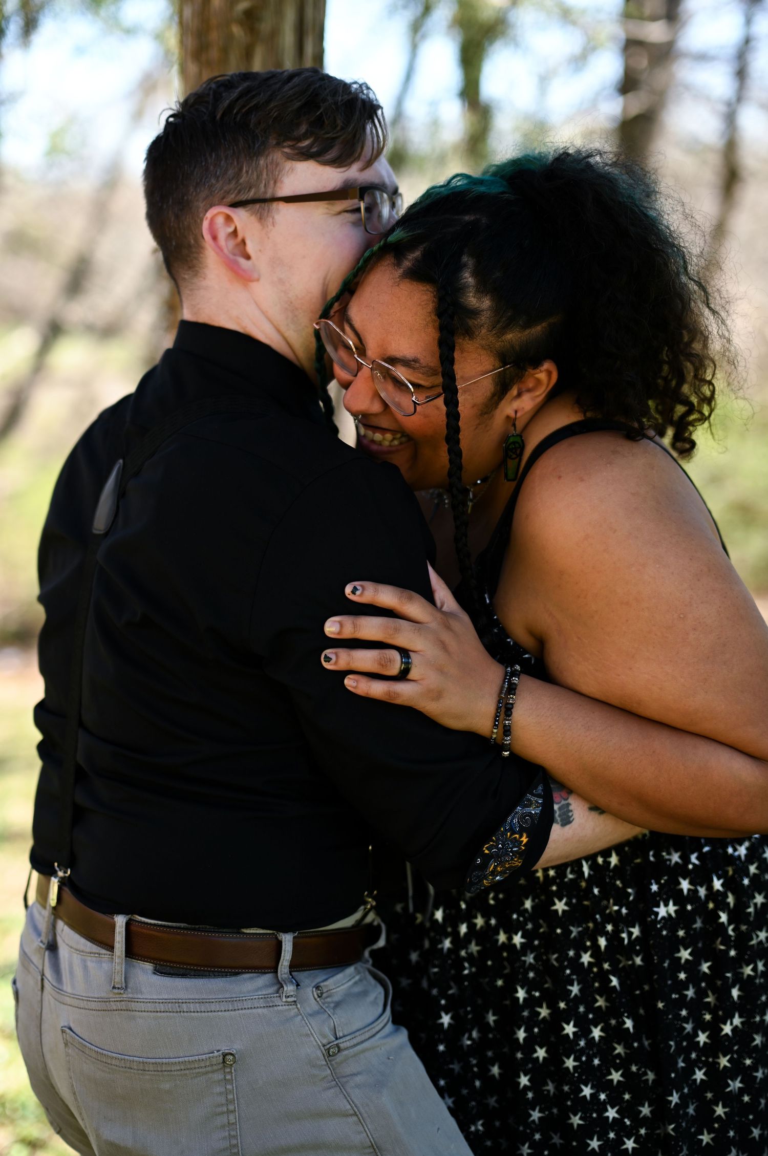 Interracial couple sharing a joyful, affectionate moment embracing outdoors near trees.