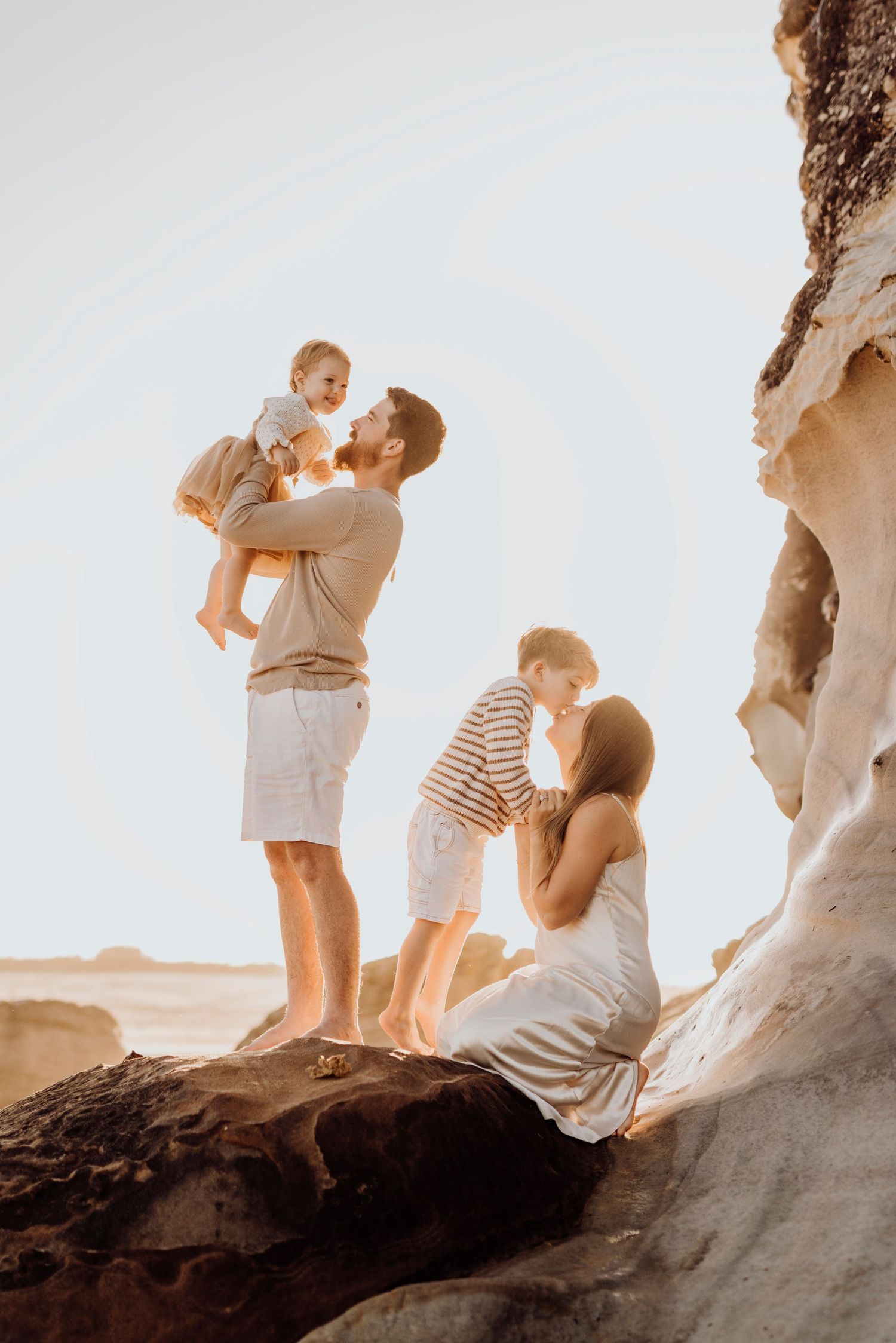 Northern Beaches family photography of parents with children standing on coastal rocks at sunset