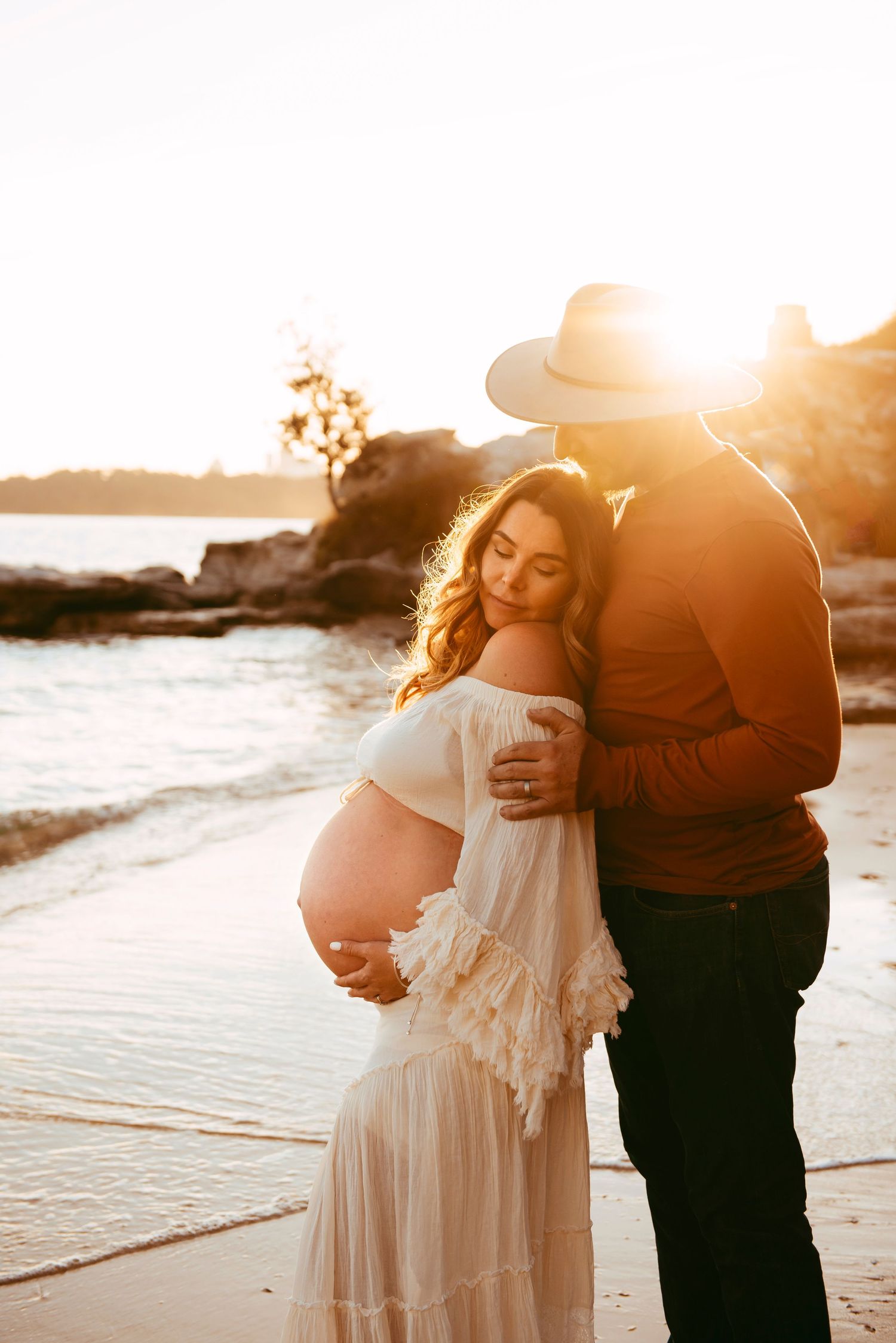 maternity photography Vaucluse Sydney of couple embracing pregnant mother at sunset on Sydney Harbour beach, rainbow baby