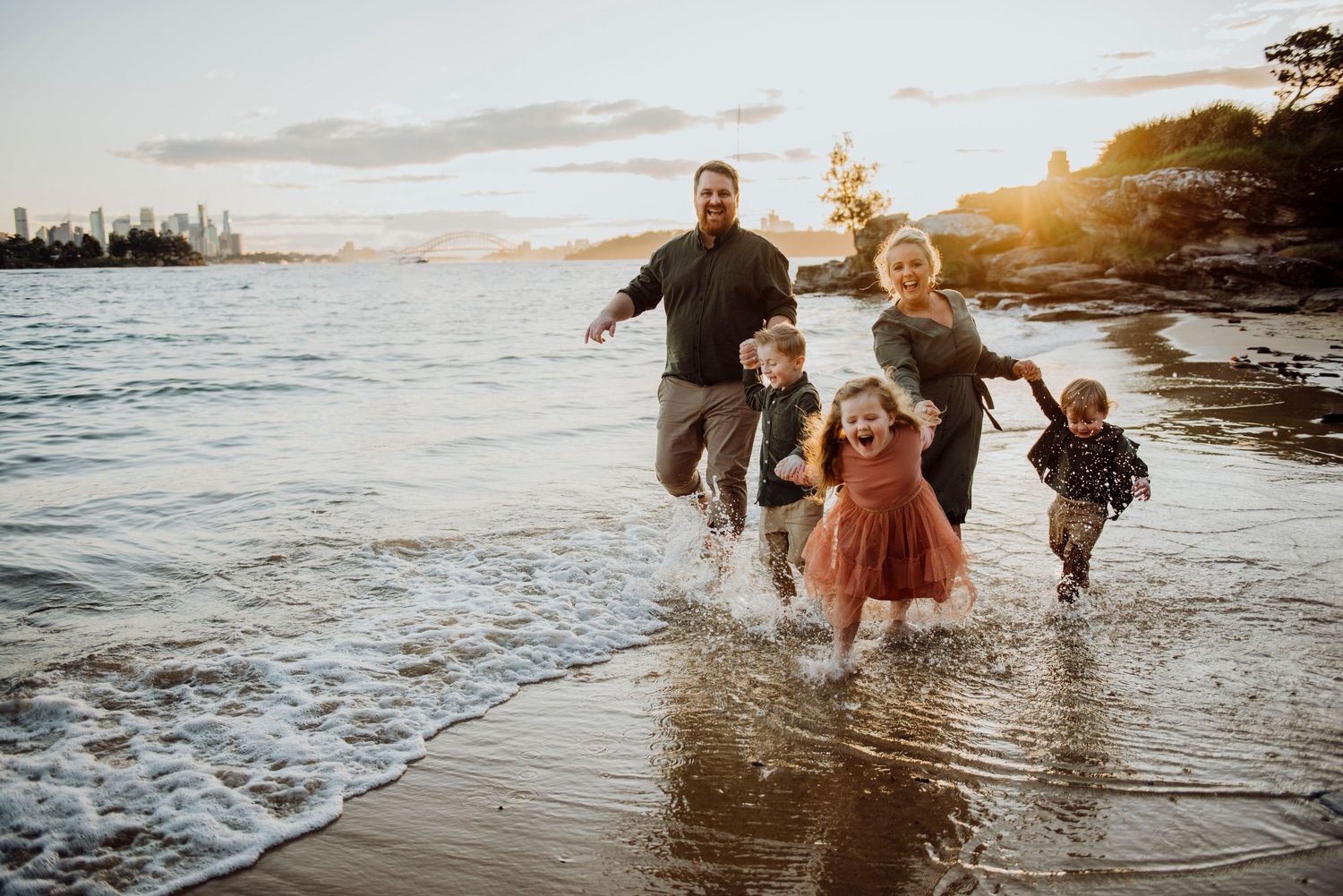 Vaucluse family photography of children running along the shoreline with parents, sydney harbour bridge in the background