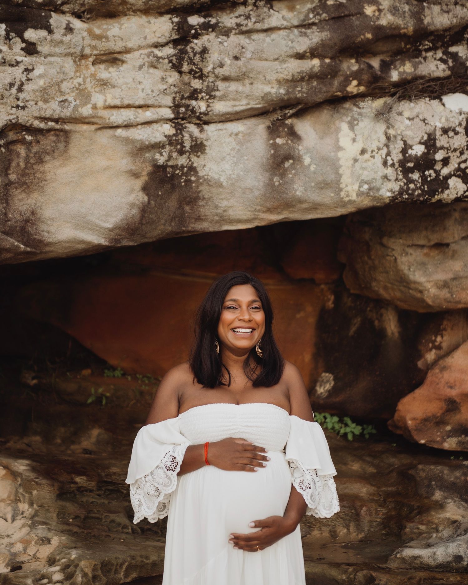 Pregnant mother in white dress photographed in Mosman Sydney against sandstone cliffs. ivf success story