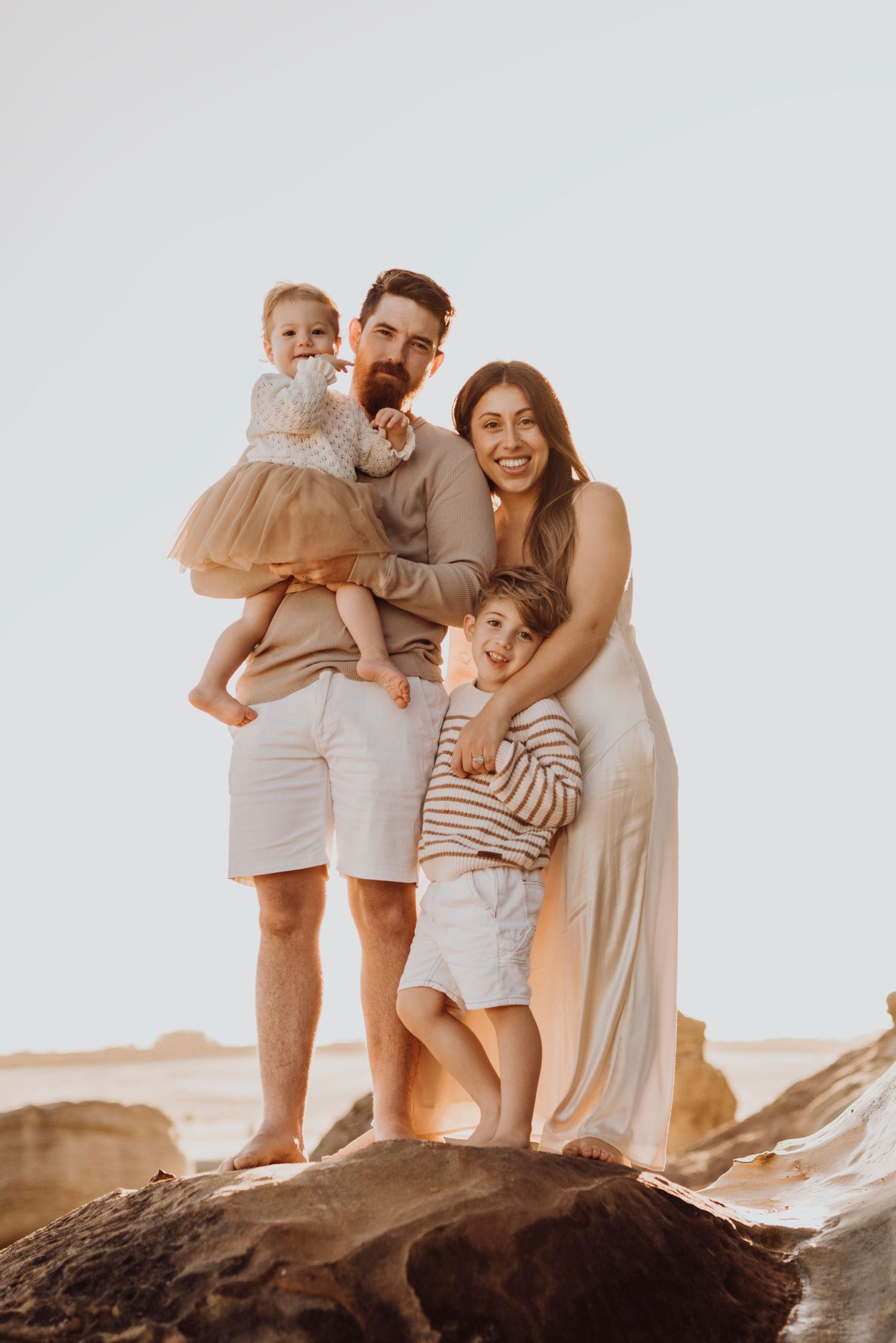 Northern Beaches family photography of parents with children standing on coastal rocks at sunset