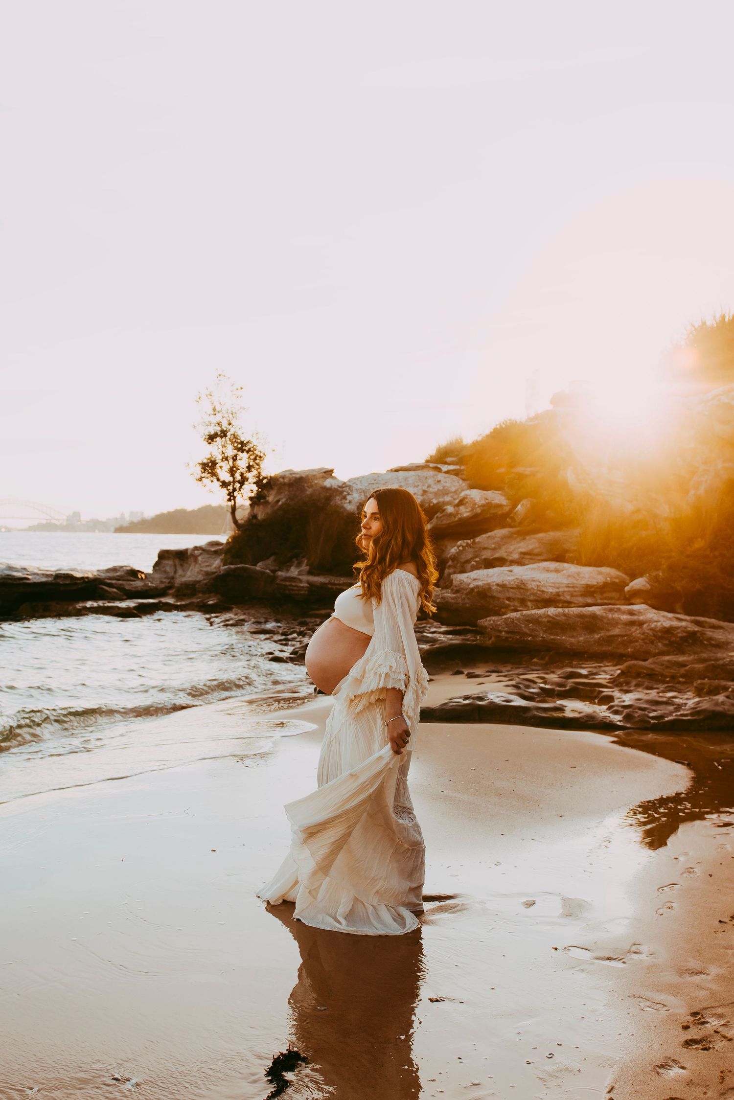 Maternity photoshoot at Vaucluse Sydney with mother walking along shoreline at sunset overlooking sydney harbour. Awaiting rainbow baby